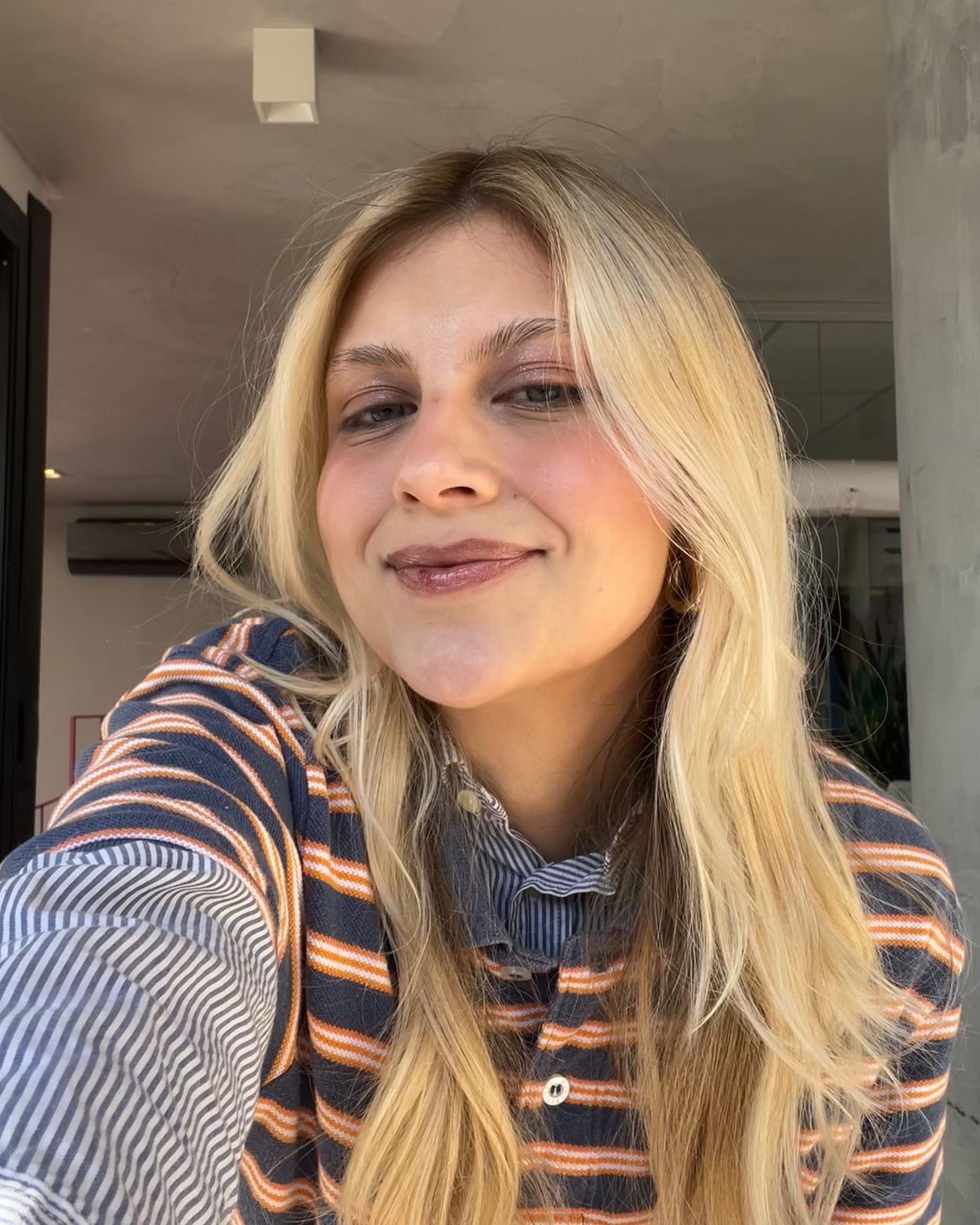 Loira sorridente com cabelo solto usando blusa listrada. Detalhe para o 