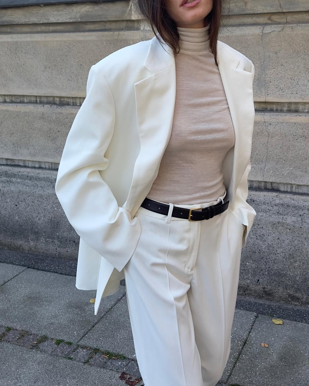 Pessoa com blazer branco, blusa preta, shorts e meia-calça, óculos escuros e sapatos estampados em ambiente urbano.