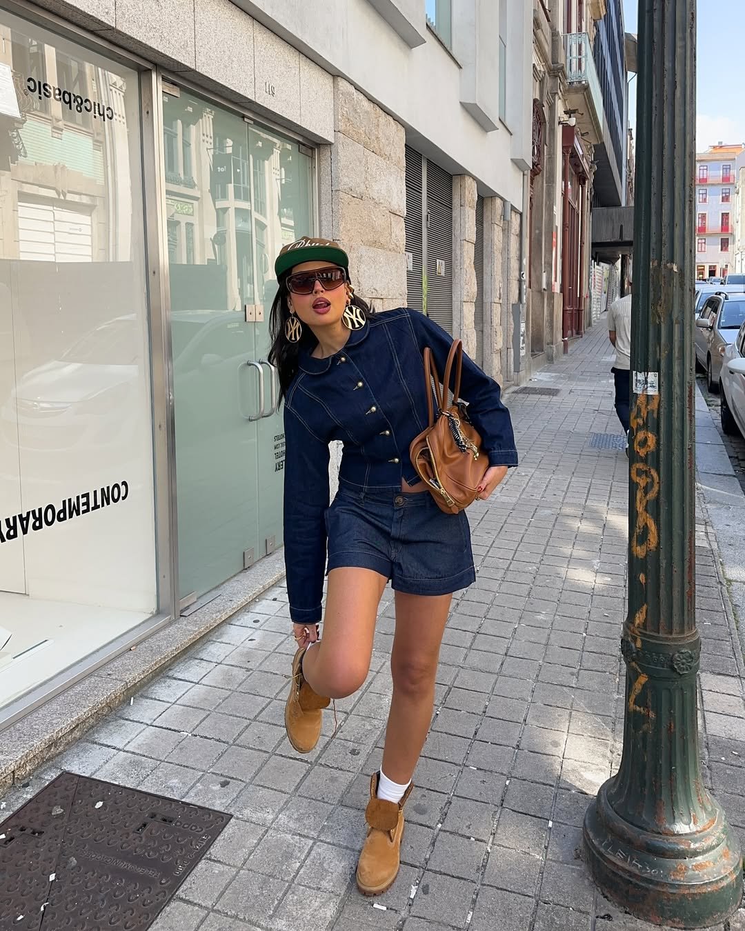 Pessoa usando jaqueta jeans e bota Timberland marrom, andando em uma calçada urbana.
