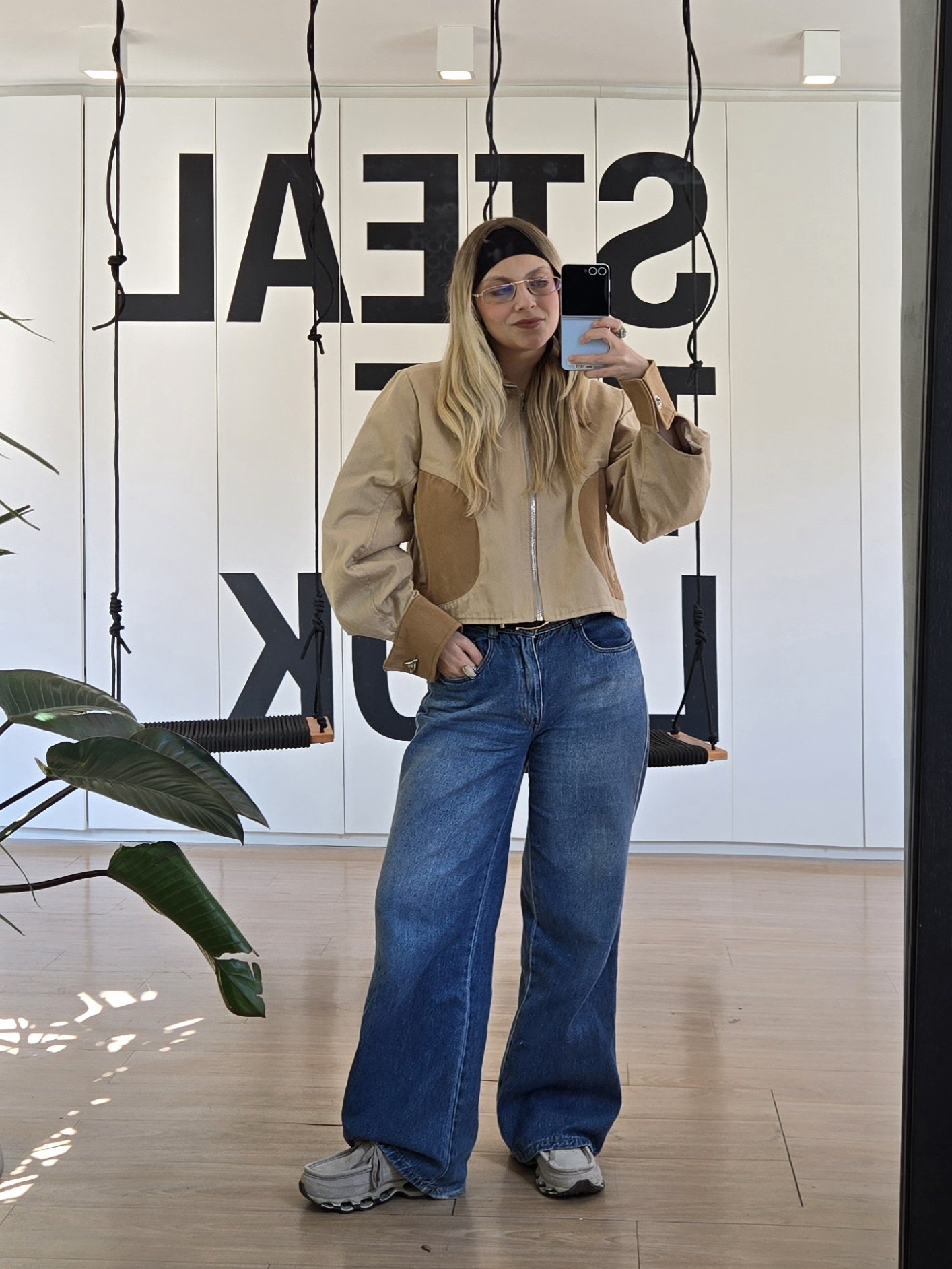 Pessoa em roupa casual reflete em espelho, veste jaqueta bege e jeans largo. Sapatos se destacam sem seguir tendência mocassim.