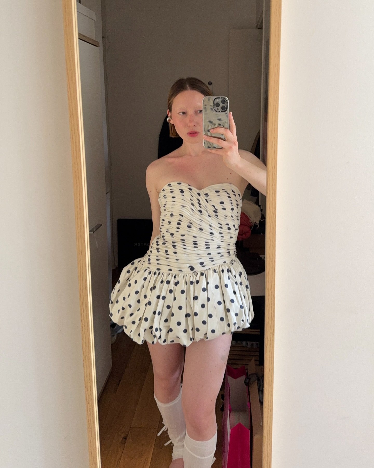 Vestido curto com estampa de bolinha pretas sobre fundo branco, usado por pessoa tirando selfie.