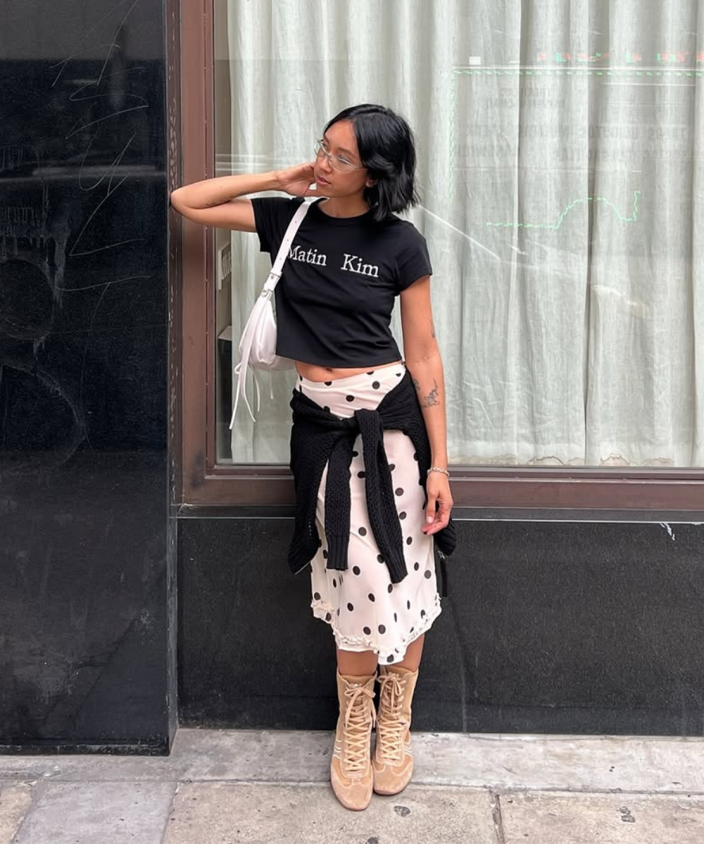 Pessoa em frente a uma vitrine, vestindo preto e branco com uma blusa preta e saia de bolinhas.