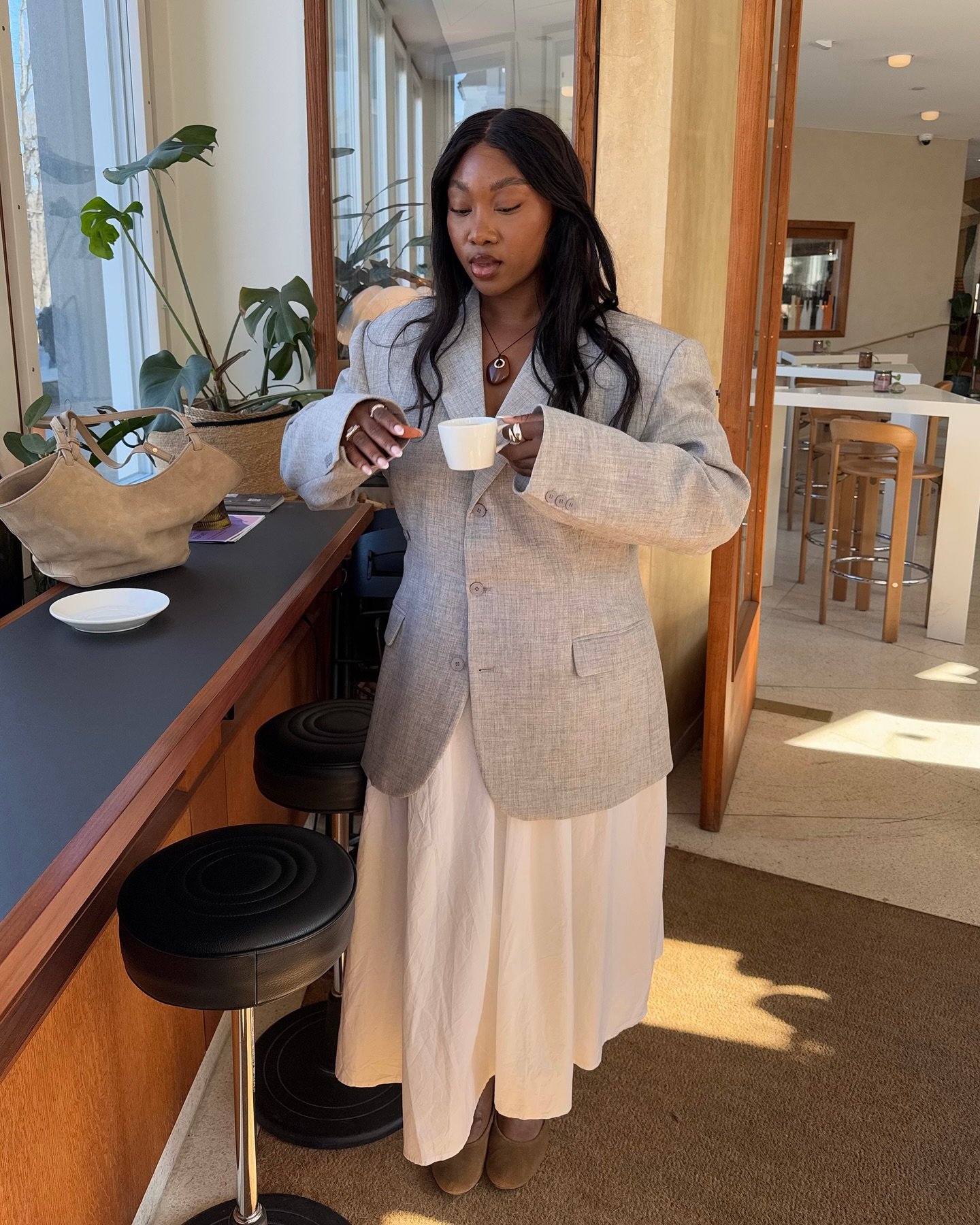 Mulher em um café usando blazer cinza e saia longa branca, combinação típica de looks de inverno com saia.
