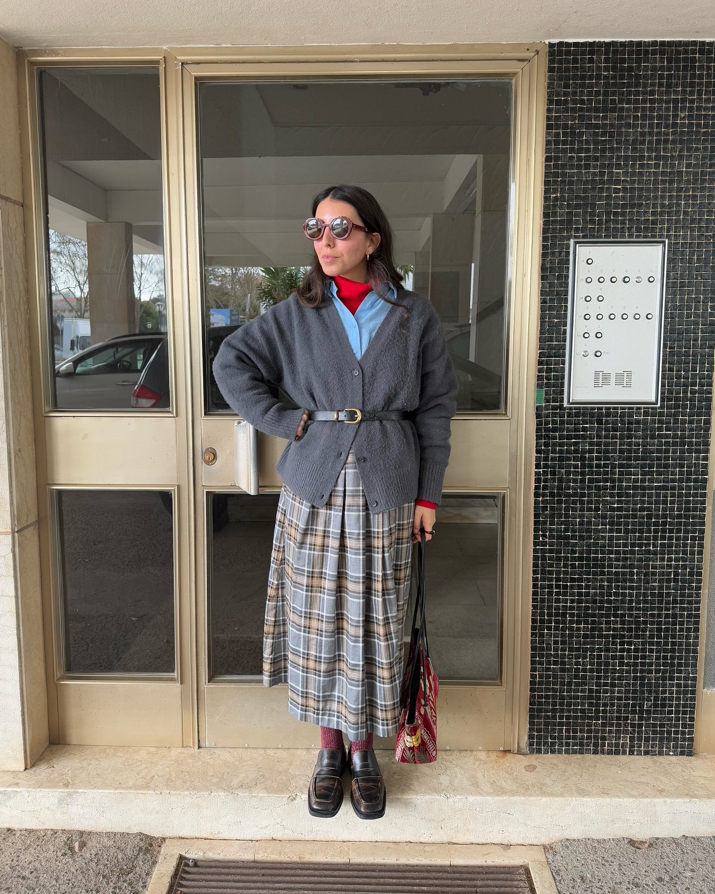 Pessoa vestindo cardigã cinza, saia xadrez e óculos de sol, combinando looks de inverno com saia.