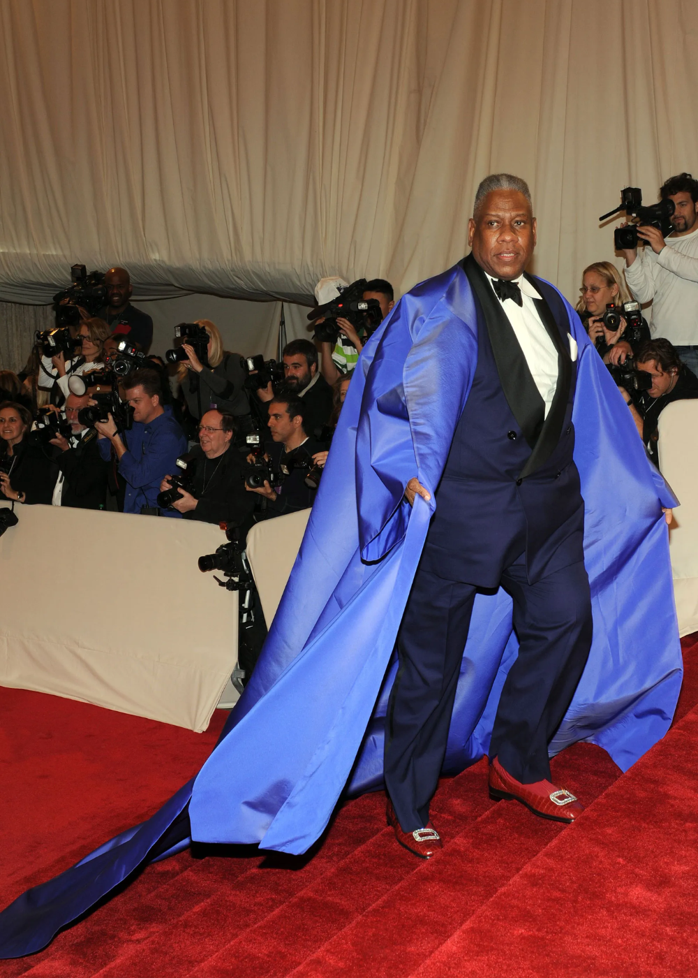 Capa azul vibrante e terno escuro realçam o visual glamouroso de um co-anfitrião, cercado por fotógrafos no Met Gala.
