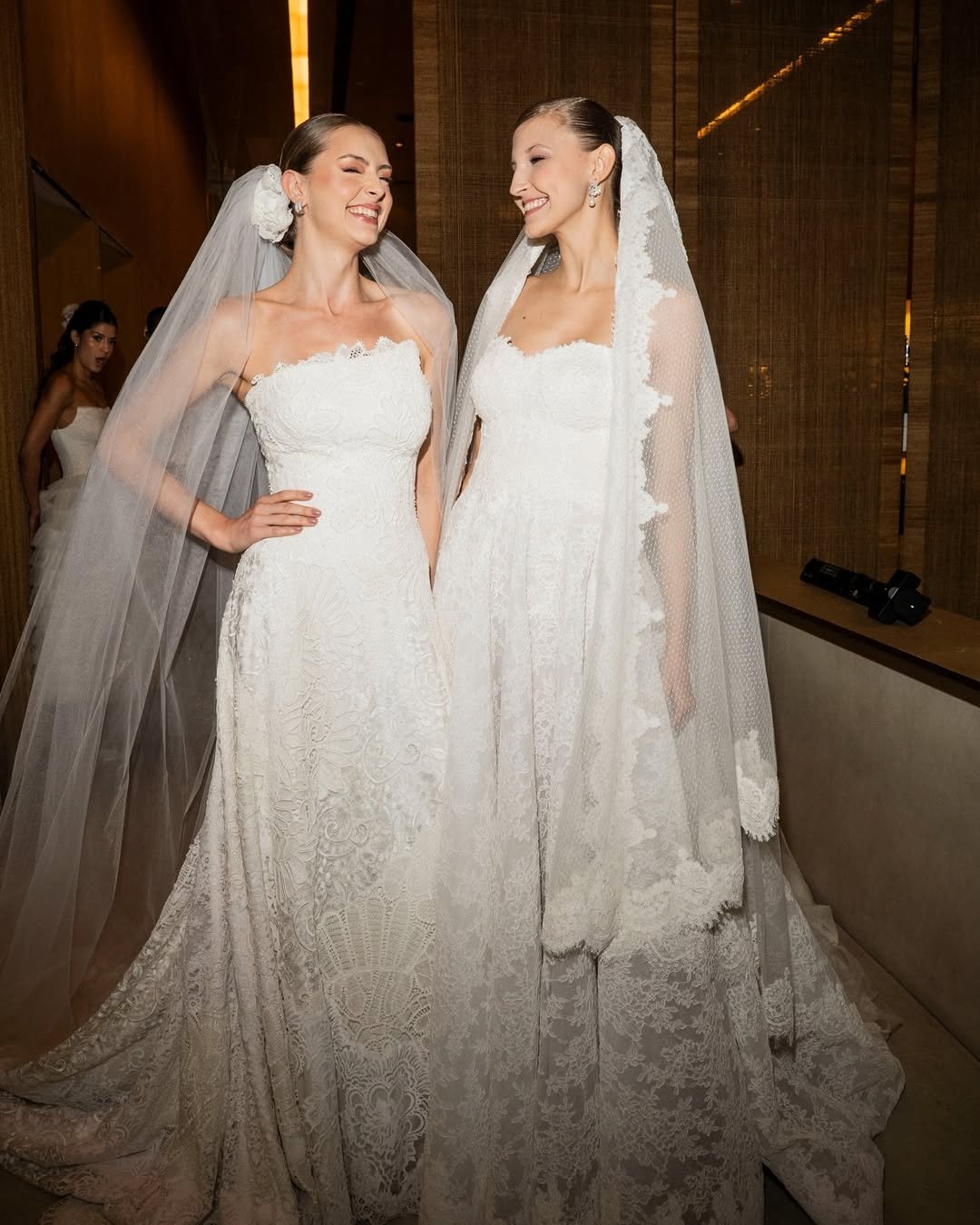 Noiva sorridente ao lado de outra em vestidos de renda, destacando elegância de Martha Medeiros.