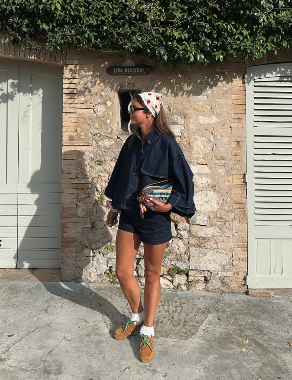 Mulher em roupa jeans, segurando bolsa colorida, com lenço na cabeça e usando tênis marrom com meias de babado.