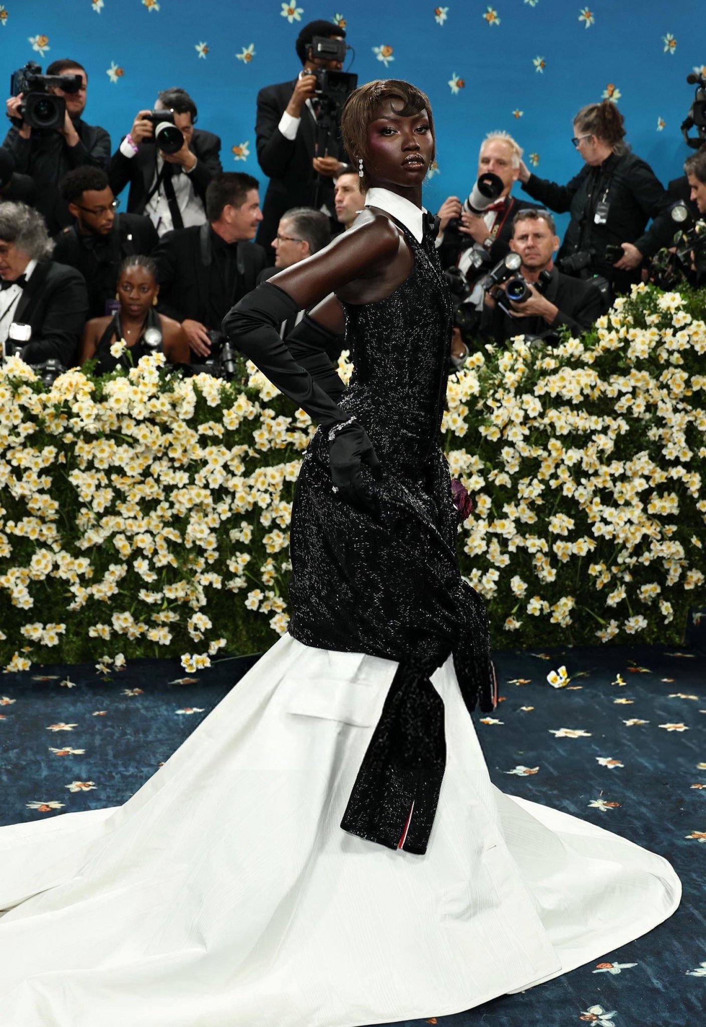 Vestido glamouroso em preto e branco no Met Gala 2025, rodeado por fotógrafos e fundo floral.