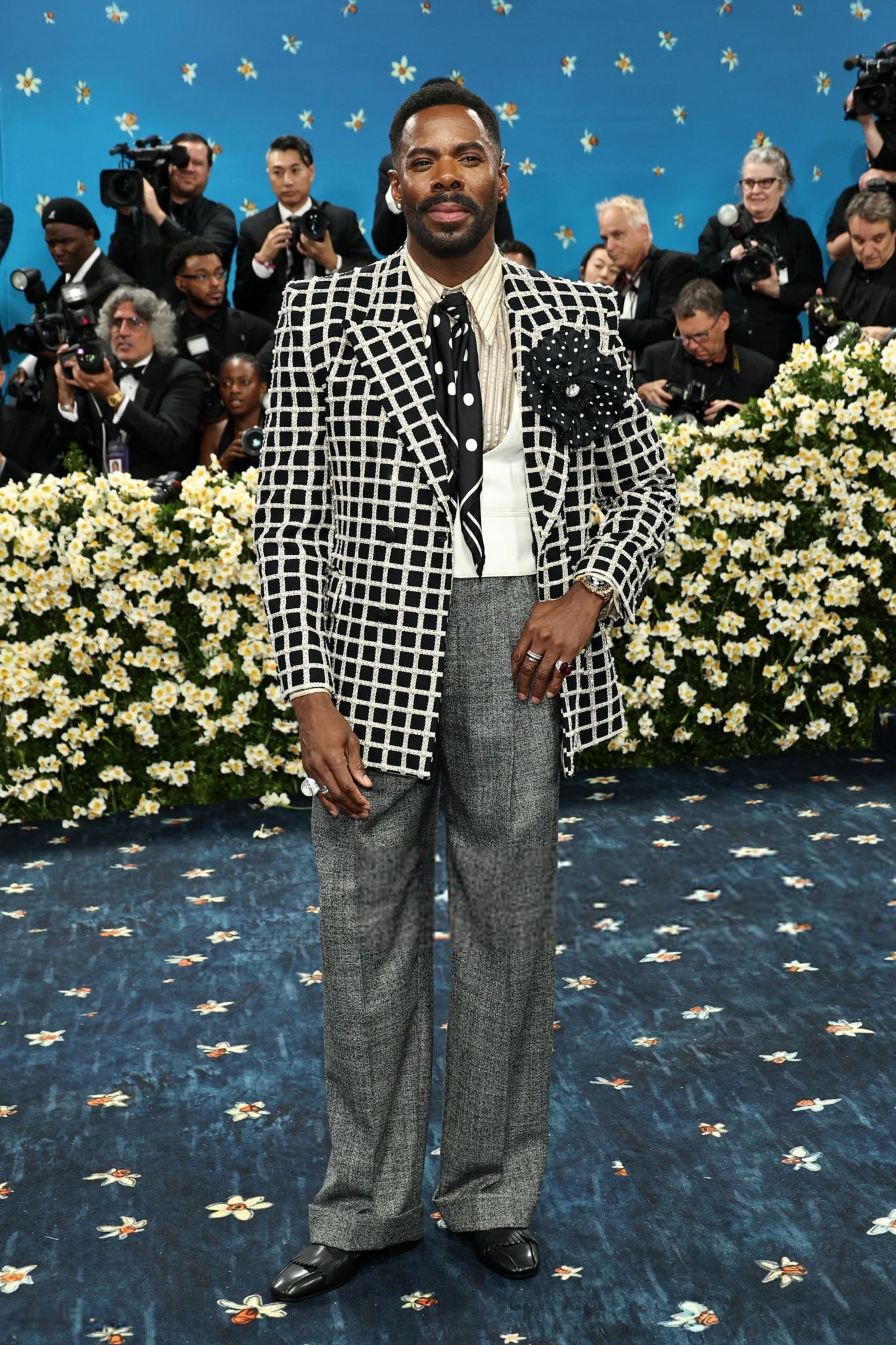 Traje elegante com paletó xadrez preto e branco, gravata preta e calça cinza, em evento com fotógrafos. Looks masculinos