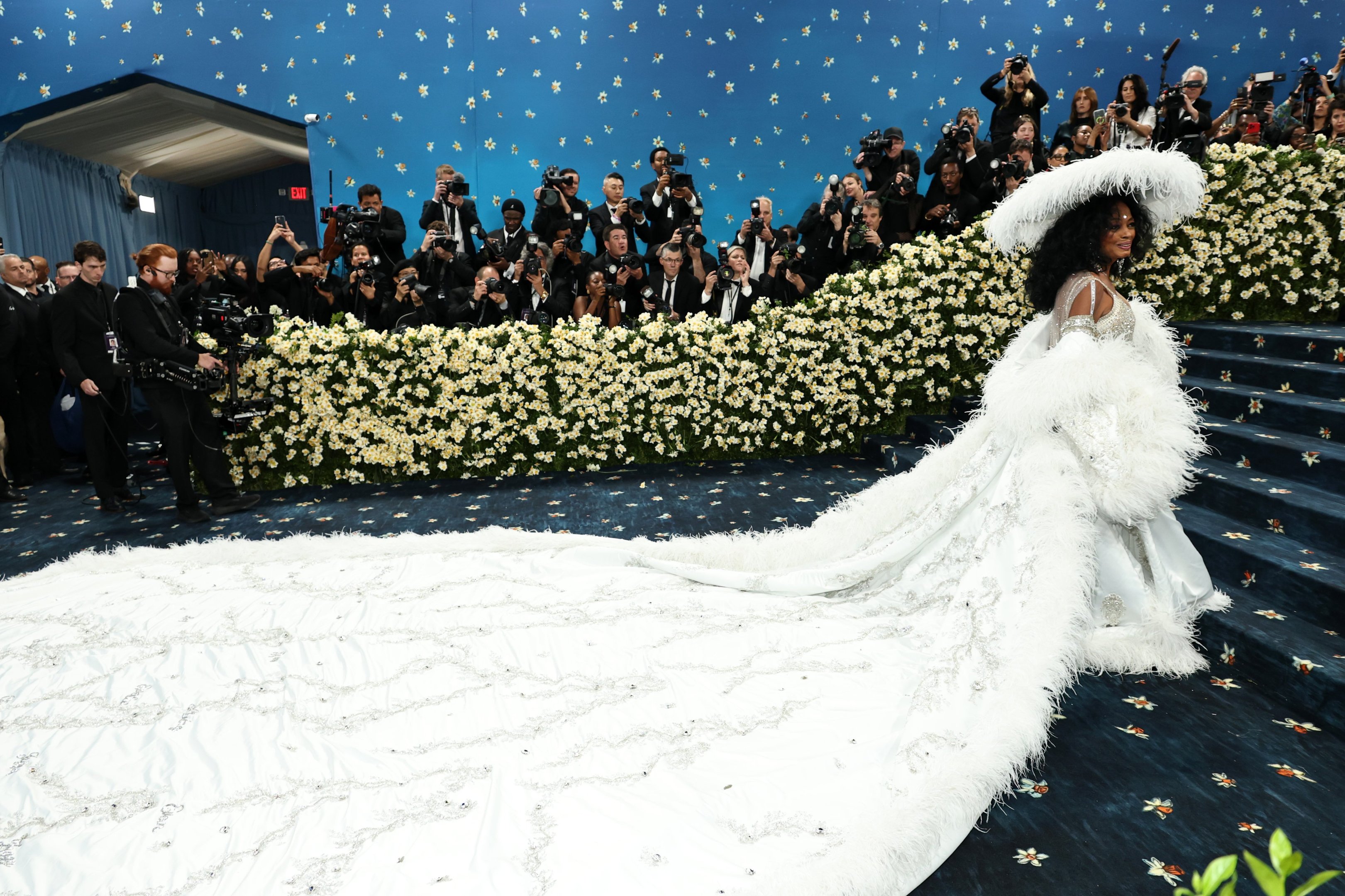Celebridade com vestido branco exuberante no tapete azul, cercada por fotógrafos no Met Gala 2025.