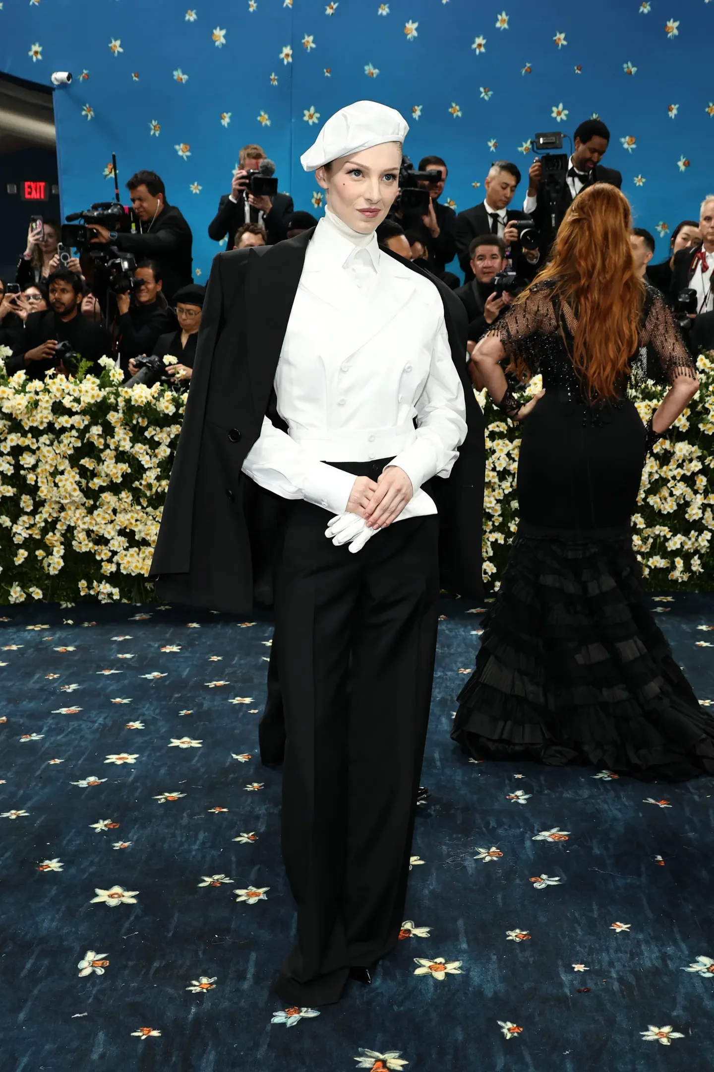 Celebridade com traje preto e branco elegante, incluindo boina e luvas, no Met Gala 2025. Evento com flores ao fundo.