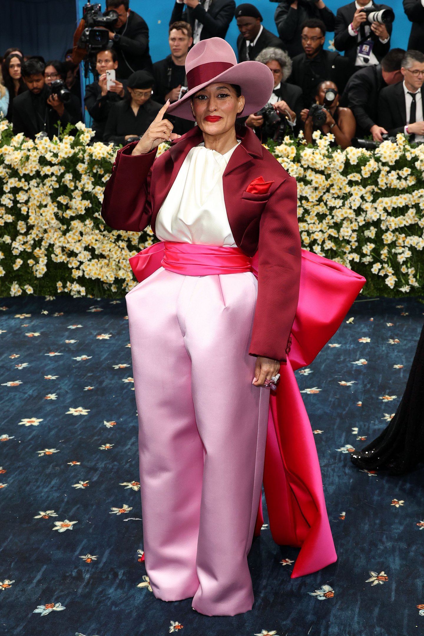 Participante vestida com terno marrom e rosa impactante no tapete azul do Met Gala 2025.