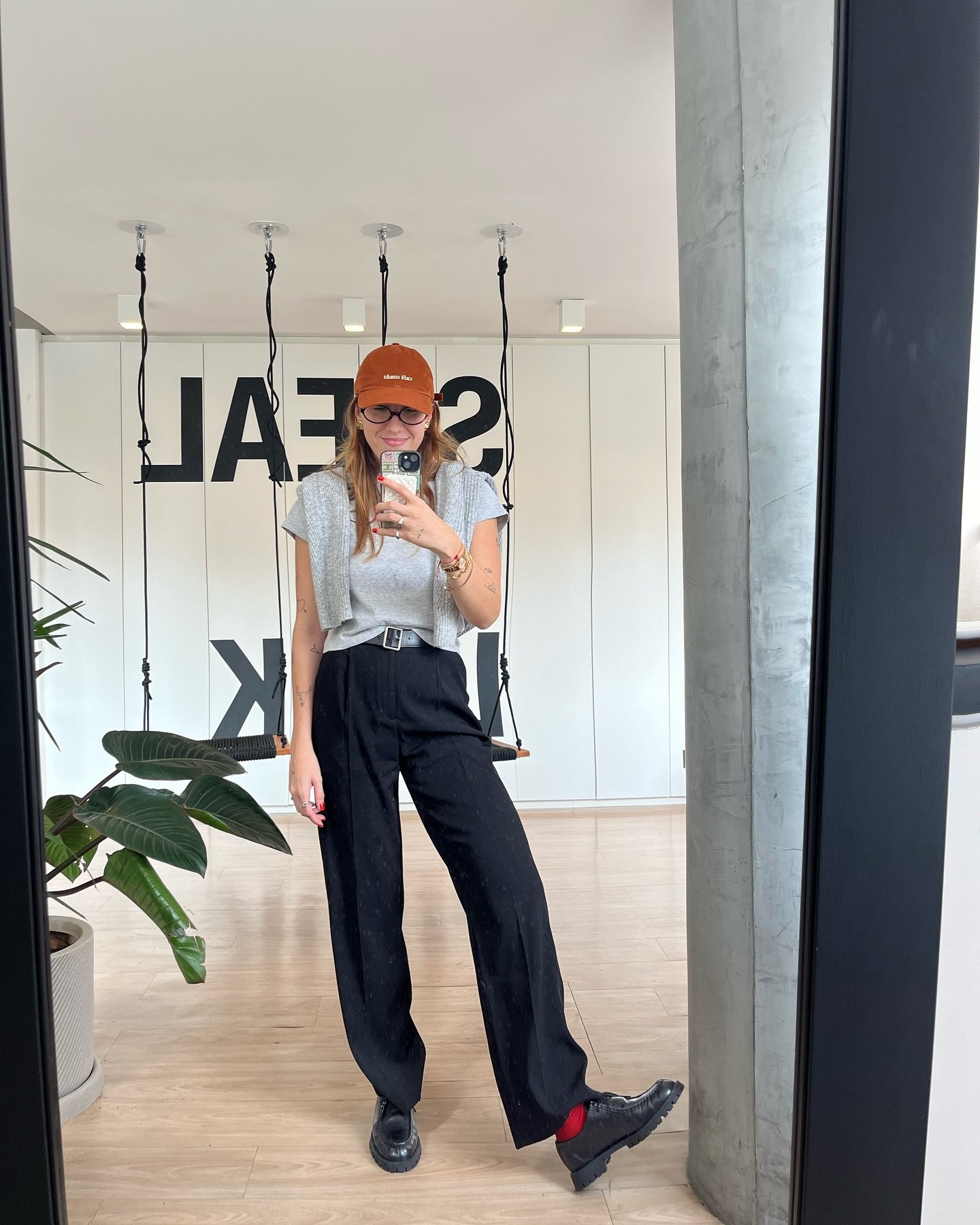 Mulher de boné tira selfie em ambiente moderno com decoração minimalista. Tema de maternidade não é aplicável.