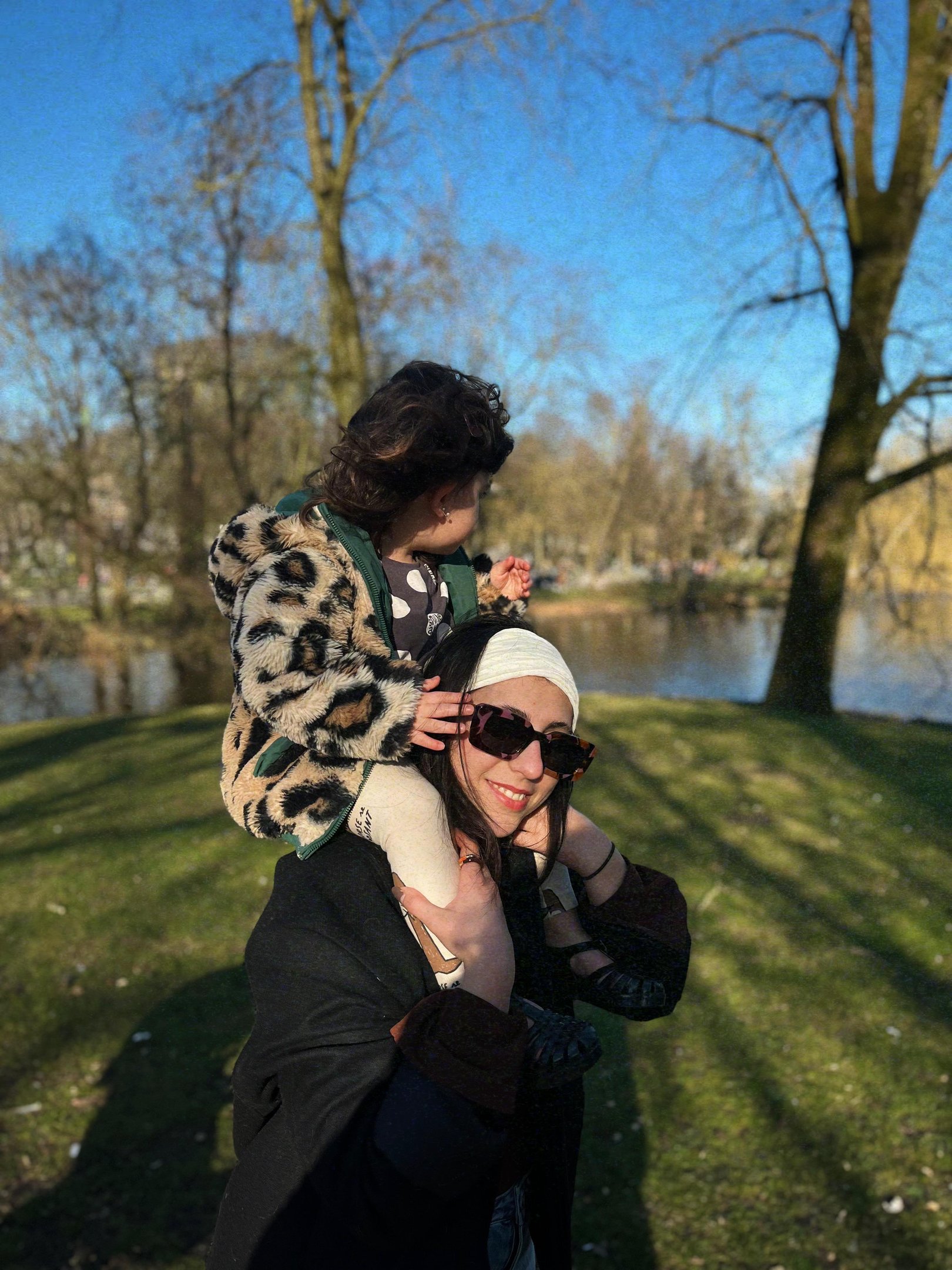 Pessoa carrega uma criança sorridente nos ombros em um parque ensolarado, simbolizando a maternidade.