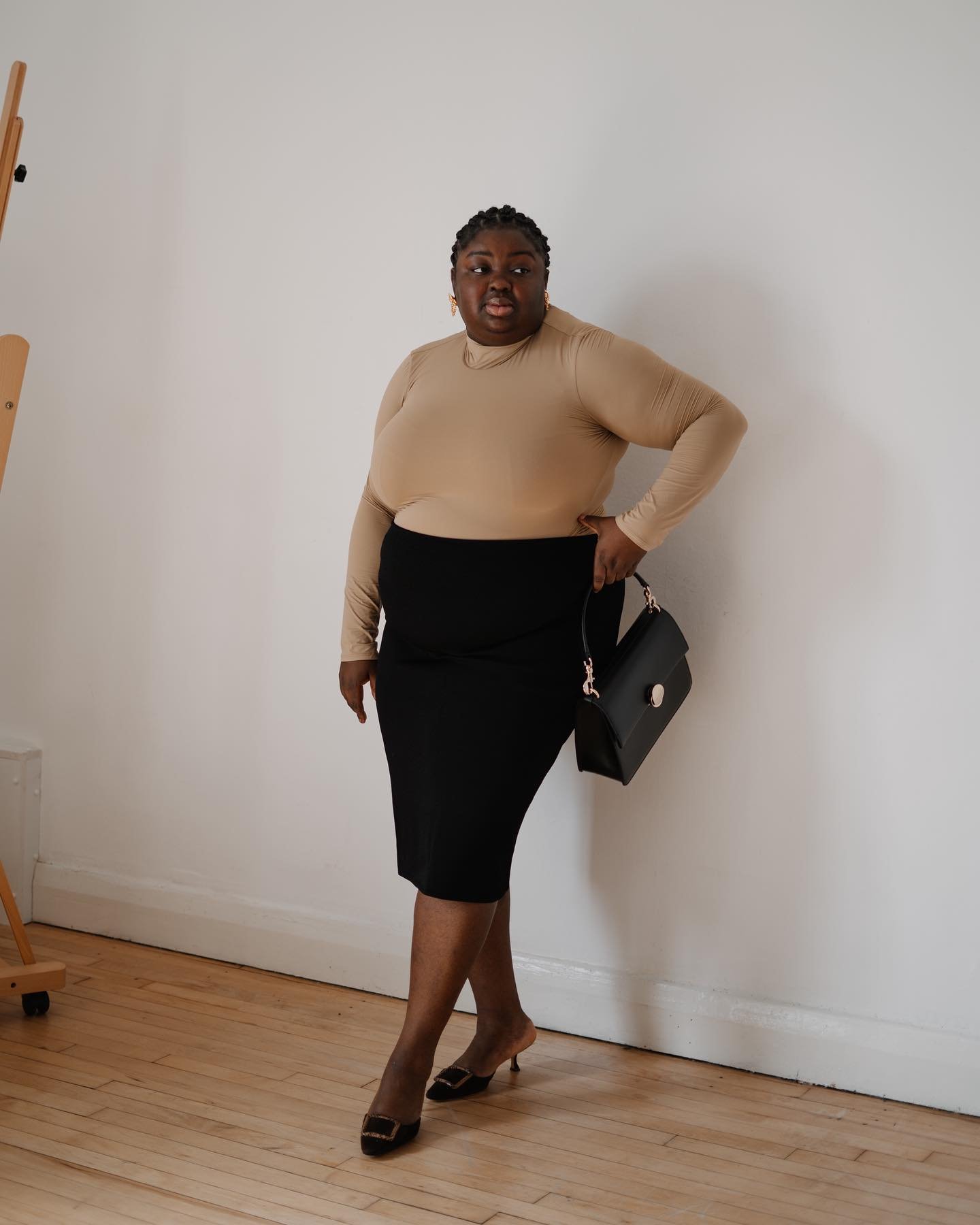 Pessoa com blusa bege e saia preta, segurando uma bolsa. Estilo alinhado à moda executiva.