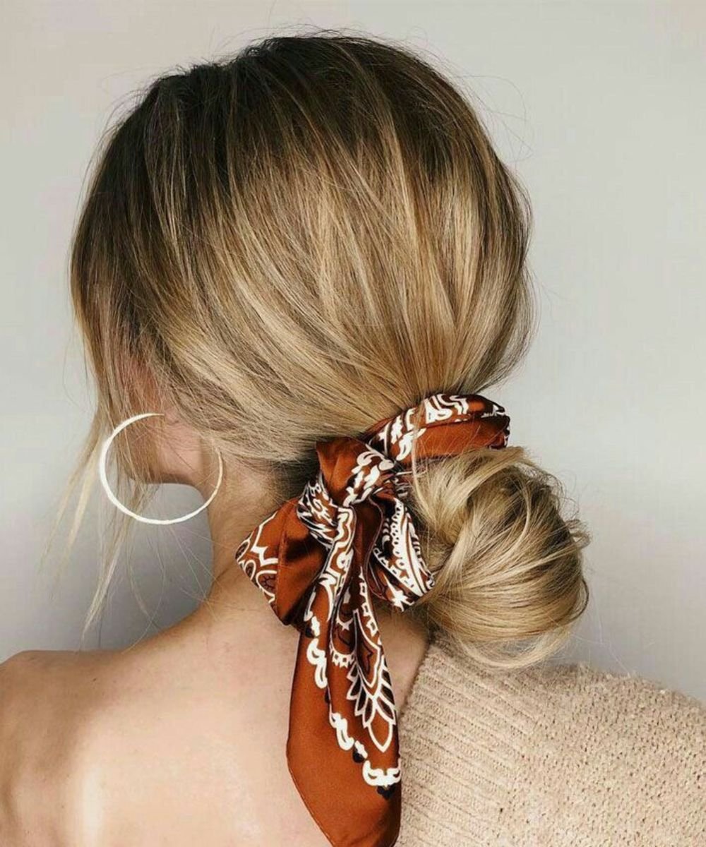 Cabelo loiro preso em coque baixo com lenço estampado, destacando penteados fáceis de se fazer.