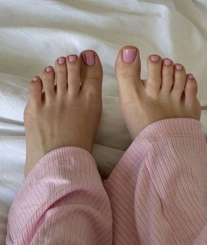 Pés macios sobre lençóis brancos, unhas pintadas de rosa, usando pijama rosa.