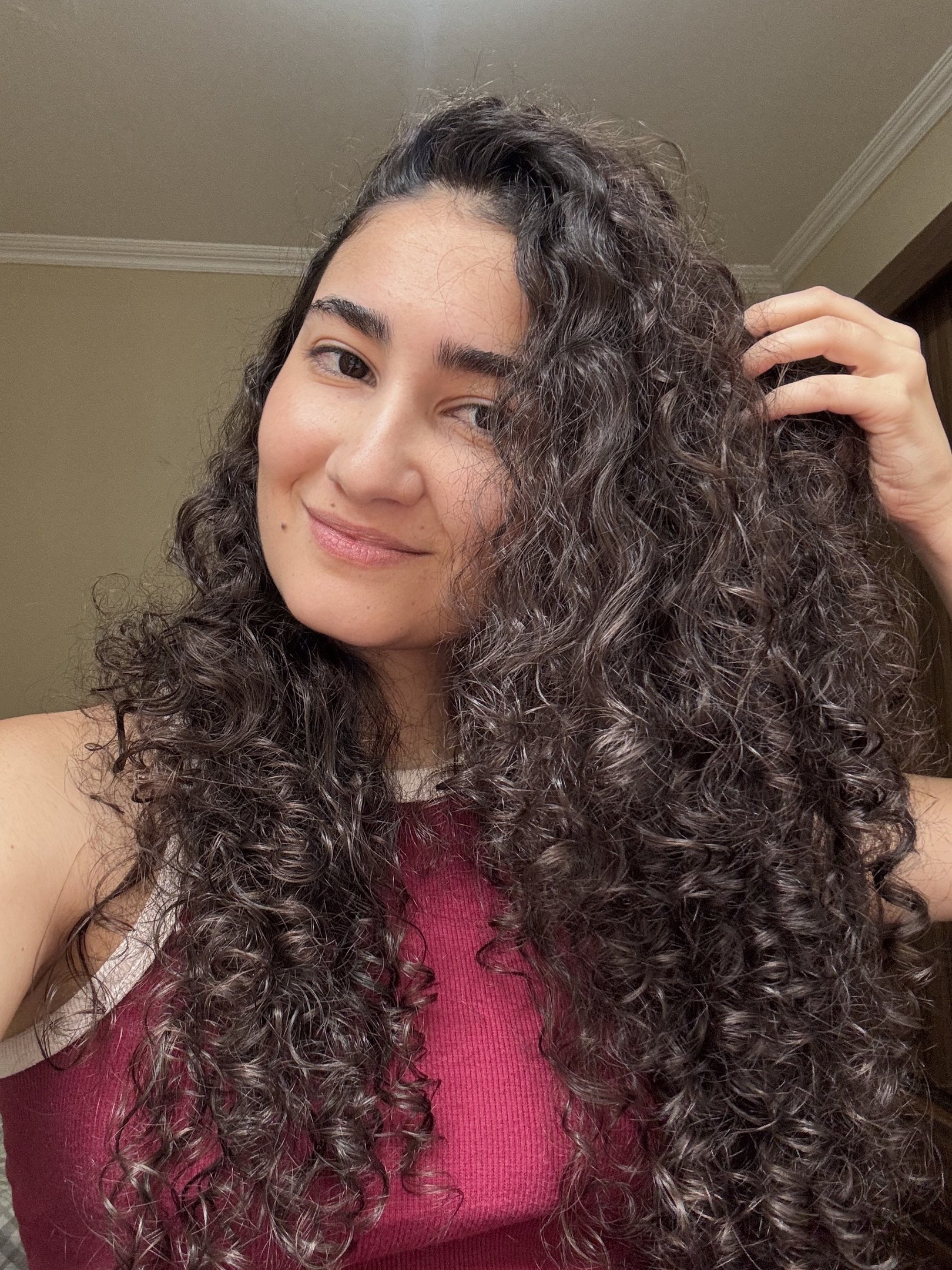 Pessoa com cabelos cacheados, aparentando estar saudável e bem cuidado, usando um primer de cabelo.