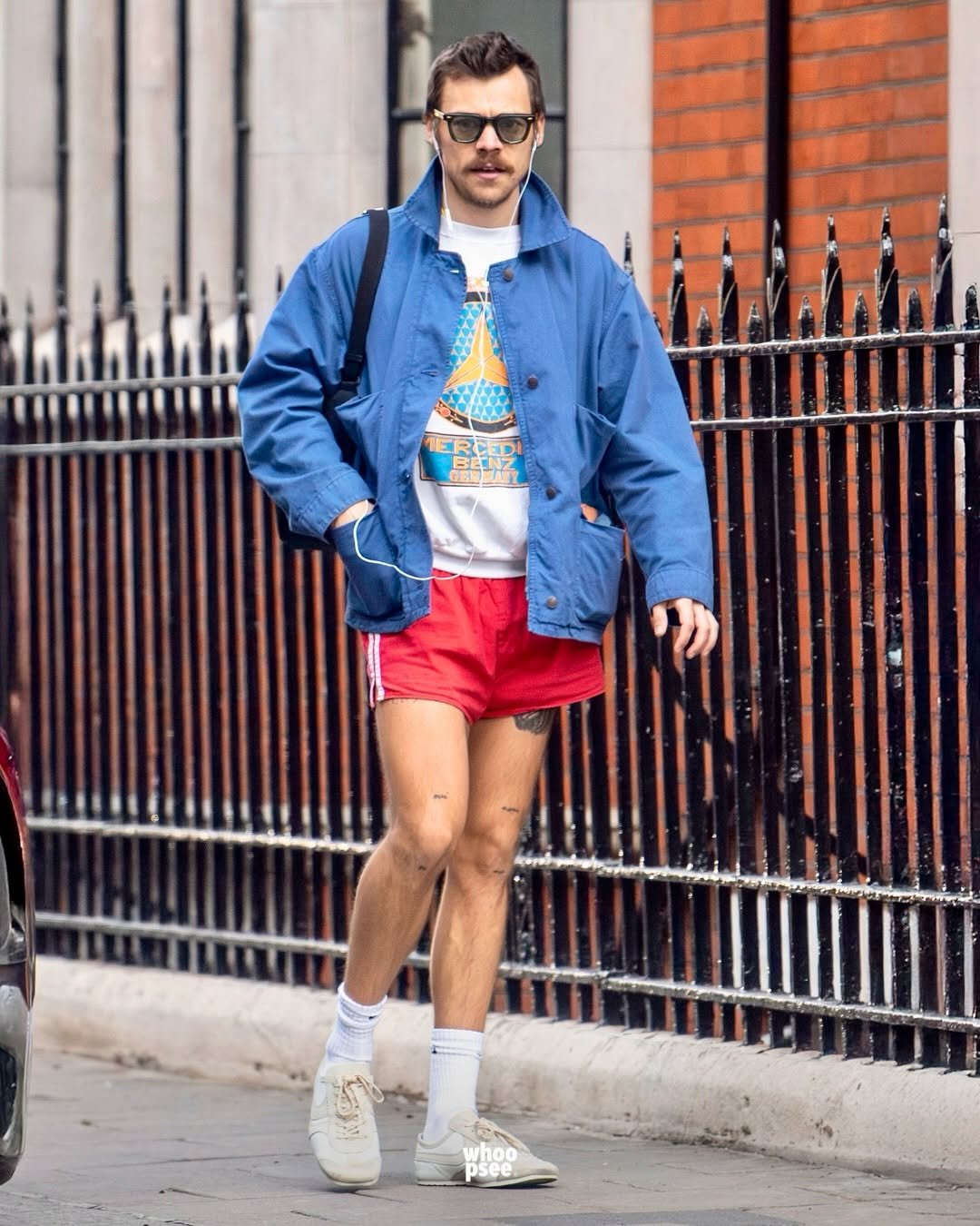 Pessoa com jaqueta azul e shorts vermelho caminha na rua com estilo descontraído. Protein chic