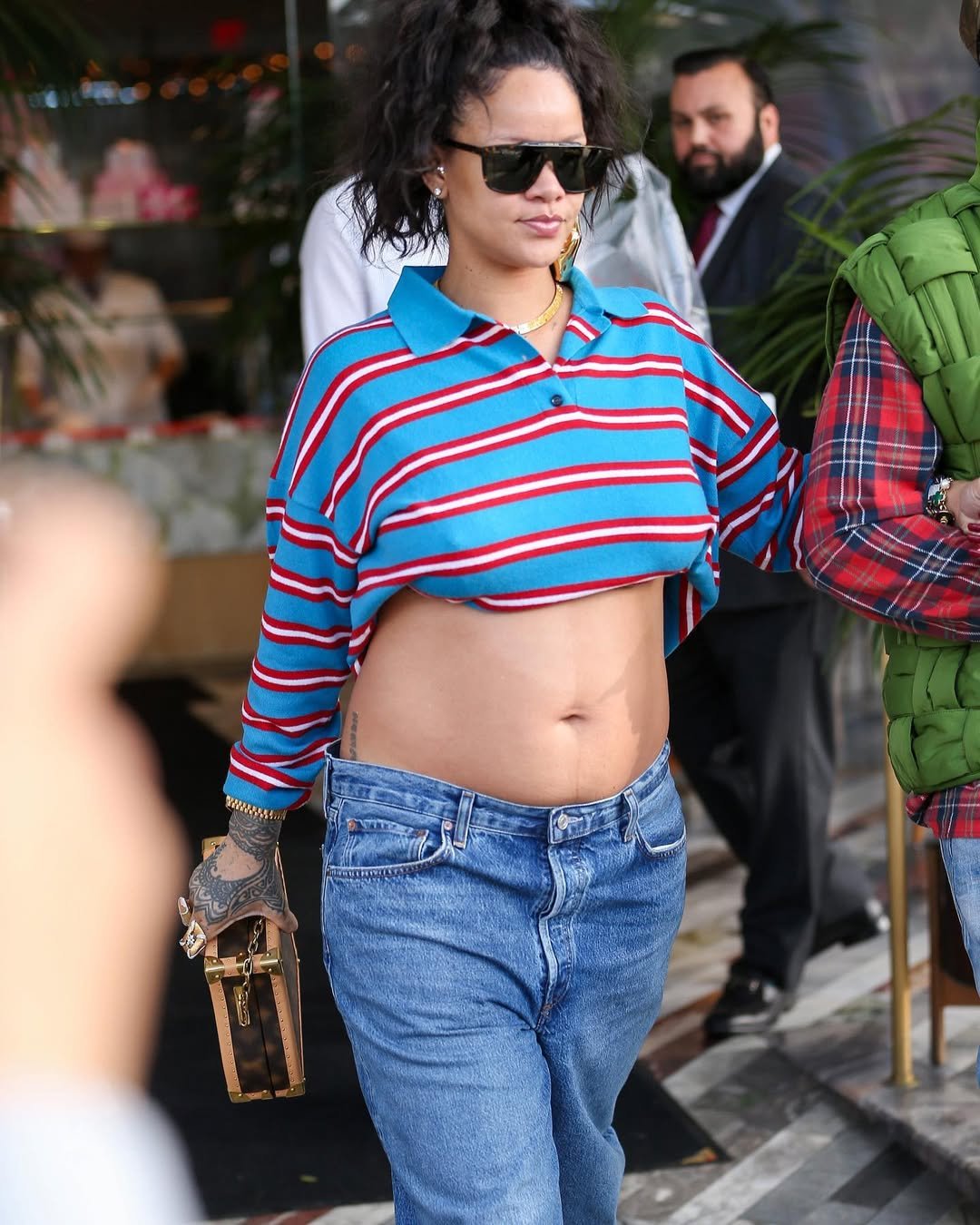 Mulher usa camisa polo listrada e calça jeans, exibindo estilo casual e tendência. Ela segura uma pequena bolsa.