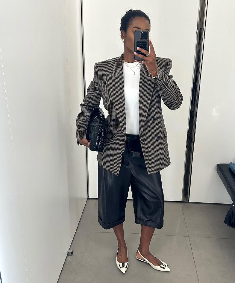 Pessoa com blazer xadrez, camiseta branca, shorts de couro fake preto e sapatilhas brancas.