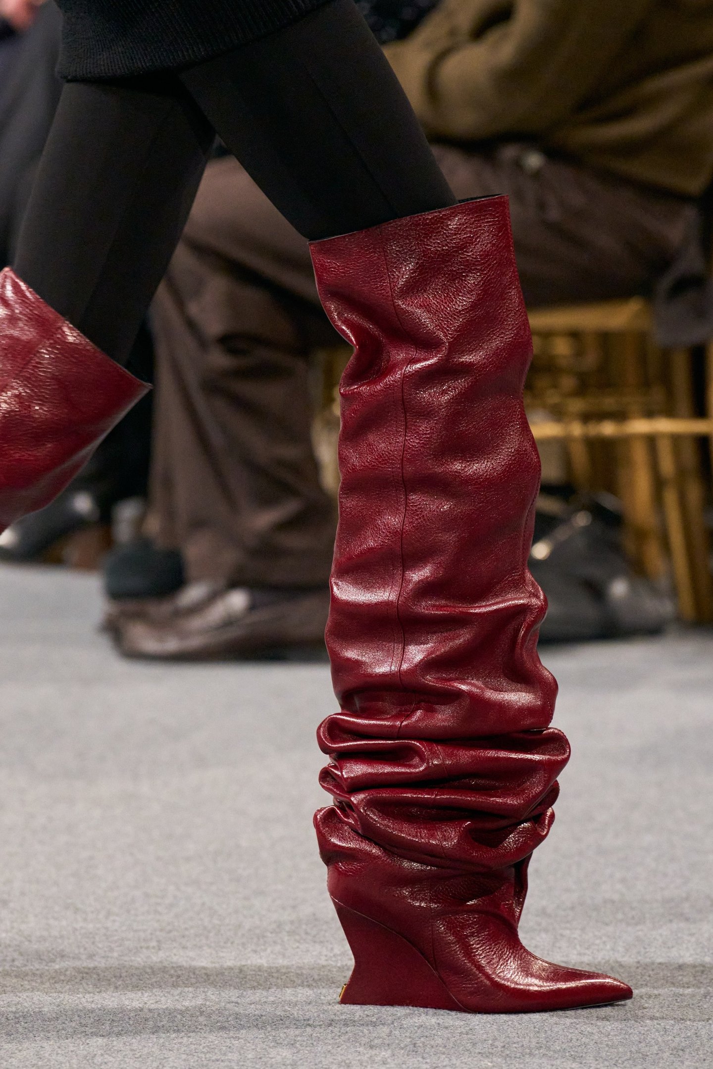 Bota vermelha de couro com salto anabela, cano alto e franzido, usada em desfile de moda.