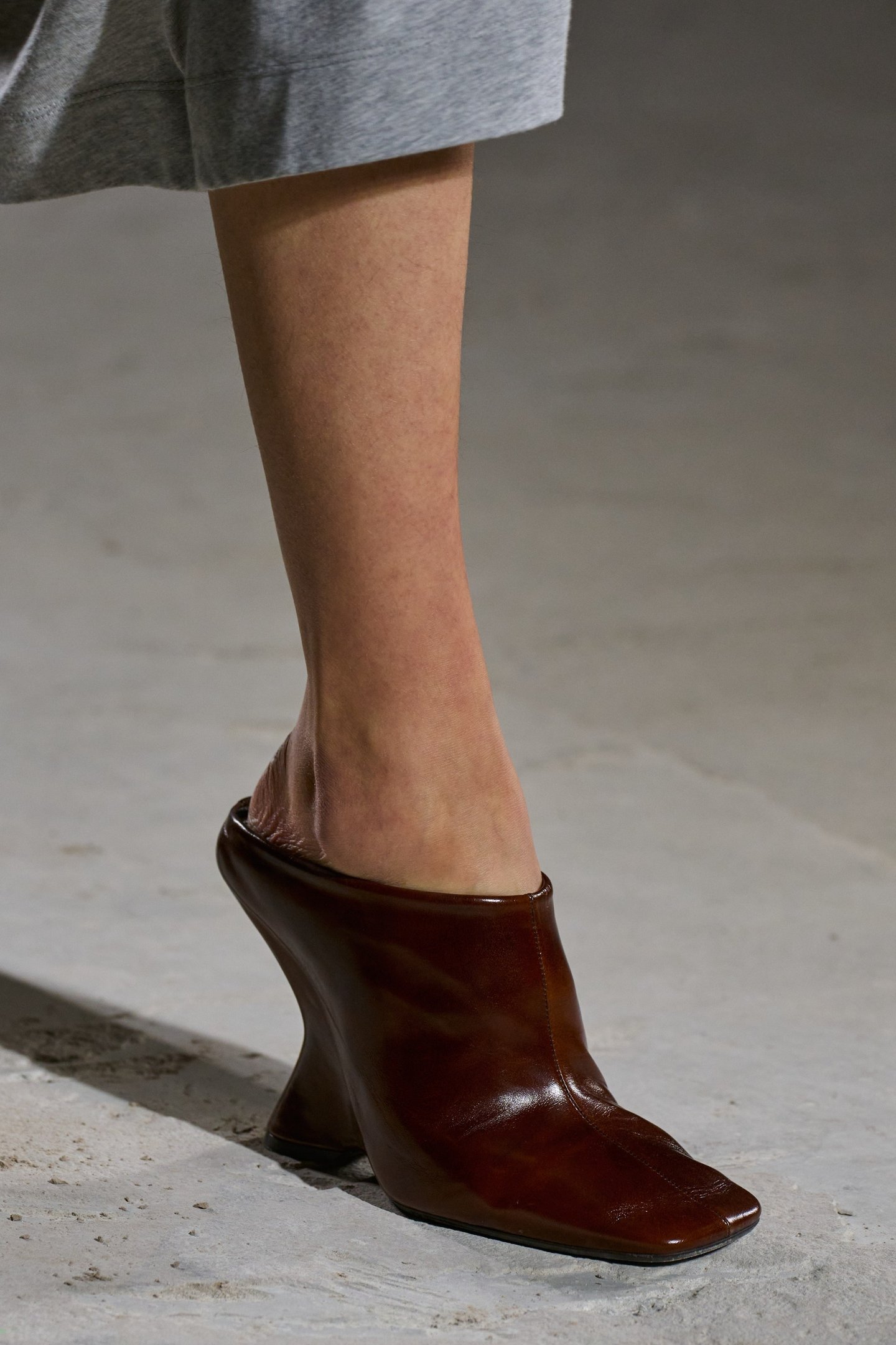 Sapato marrom de salto alto e largo, com design inusitado, usado com calça cinza.