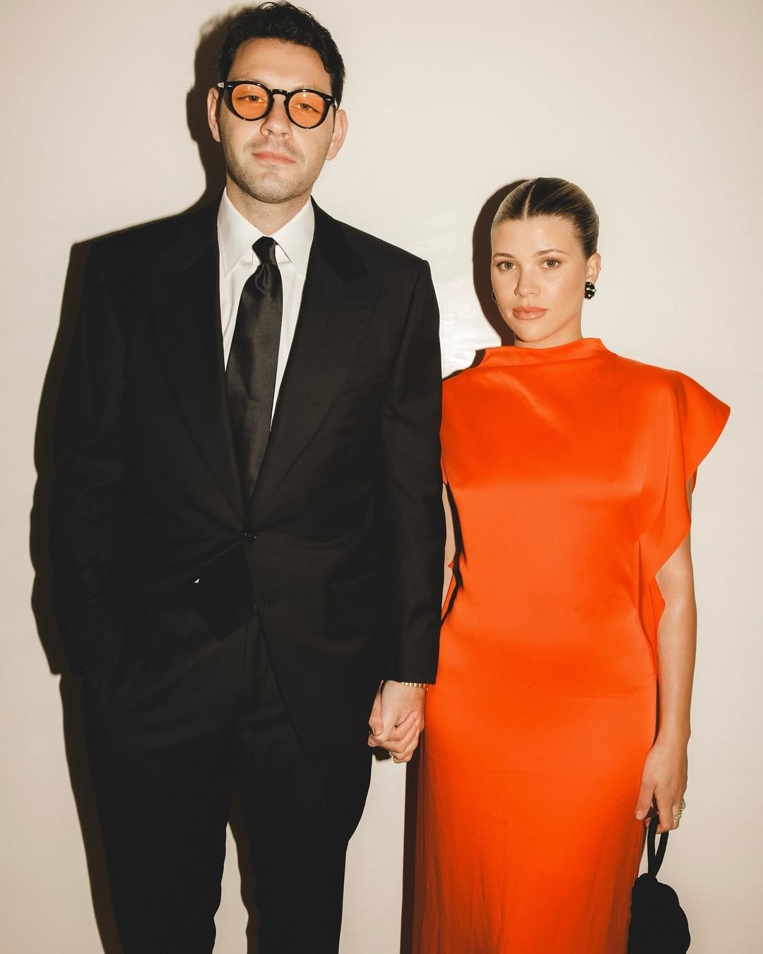 mulher usando vestido laranja e homem de terno com um dos perfumes masculinos para presentear, posando para a foto juntos