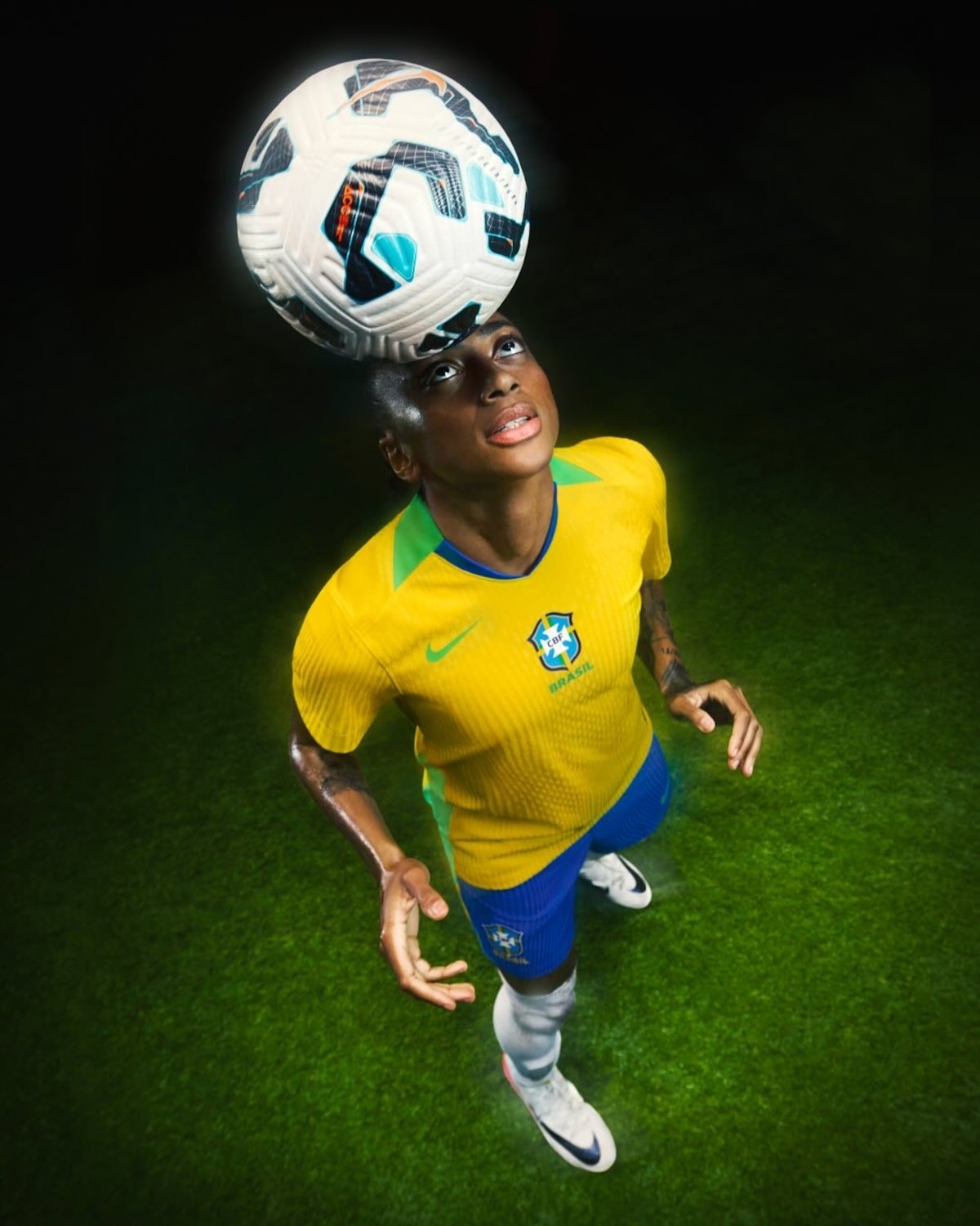 Jogador de futebol brasileiro cabeceia a bola usando chuteira de cravo, sobre campo verde.