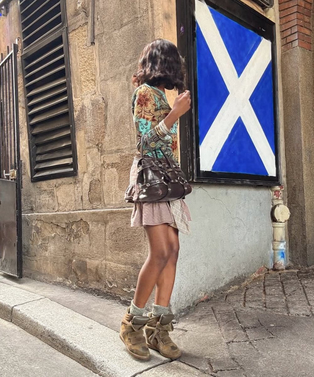 Mulher com bolsa marrom caminha ao lado de parede com cartaz da bandeira da Escócia.