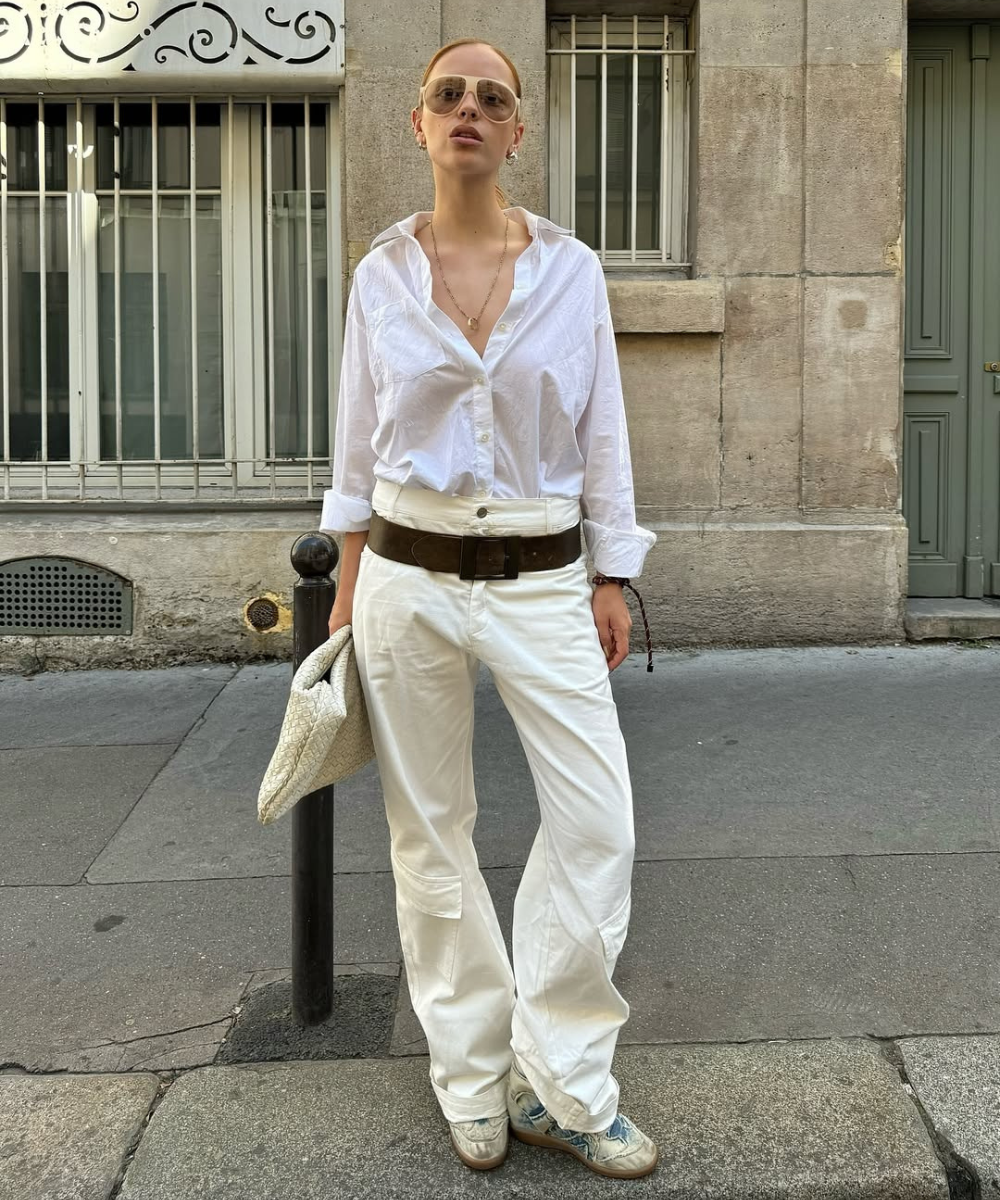 Pessoa usando camisa branca, calça larga e segurando bolsa e usa tênis de salto alto.
