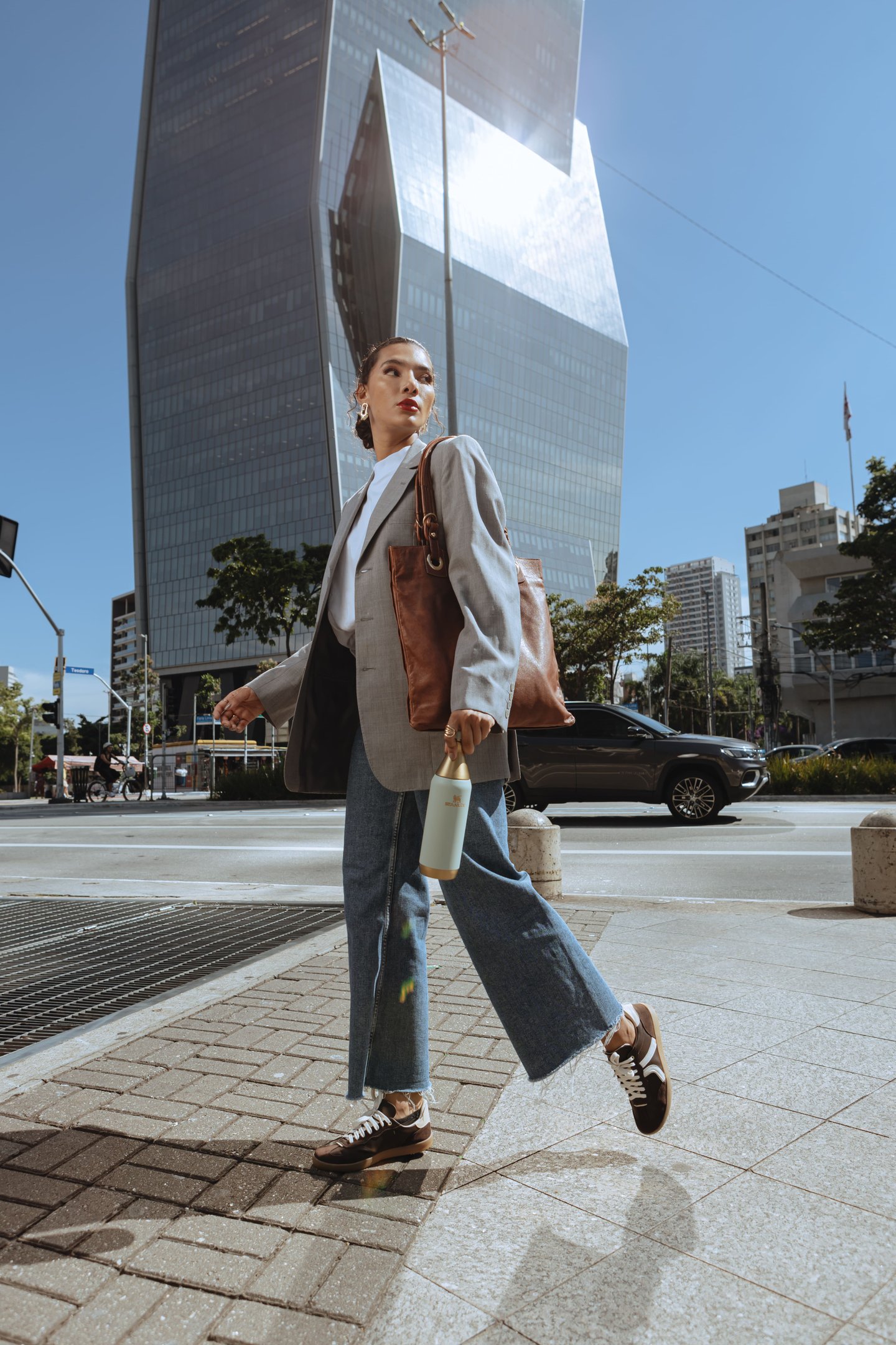 modelo de jeans, blazer e bolsa marrom e acessório funcional  - garrafa térmica