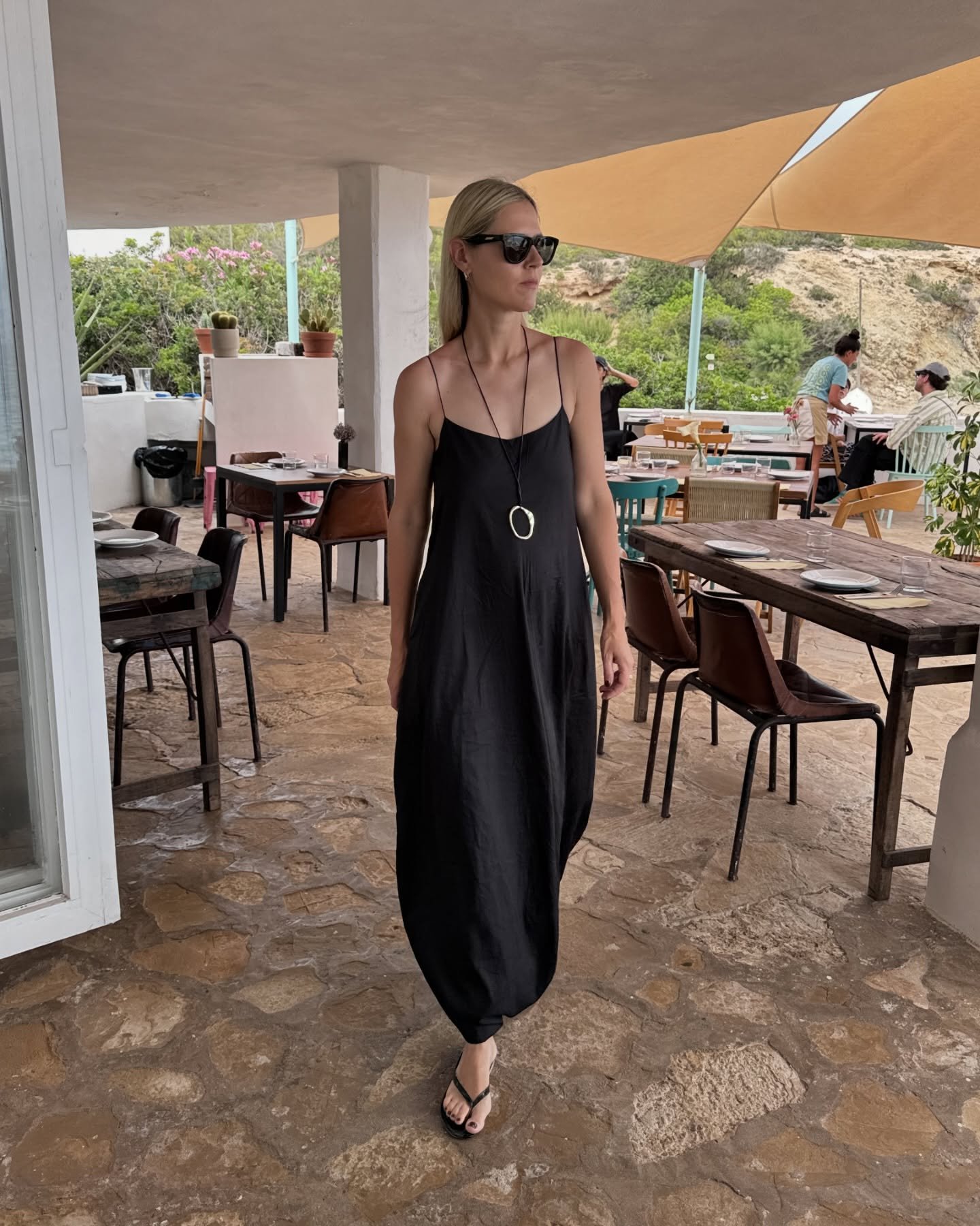 Pessoa em vestido preto, óculos escuros e colar oval, exemplificando tendência de acessórios.