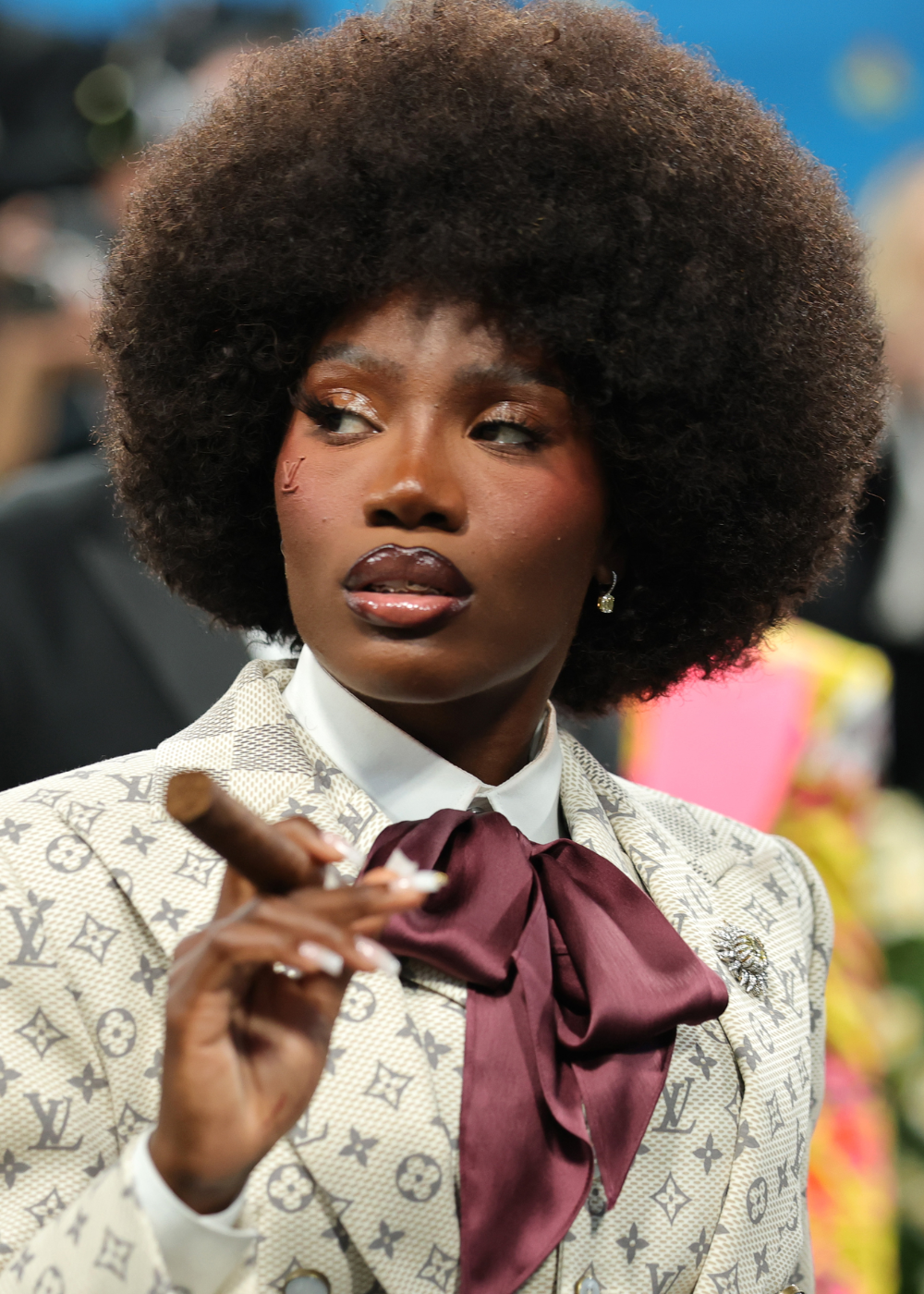 Pesssoa no Met Gala 2025, vestindo terno elegante com lenço vinho, segurando charuto, cabelo afro.