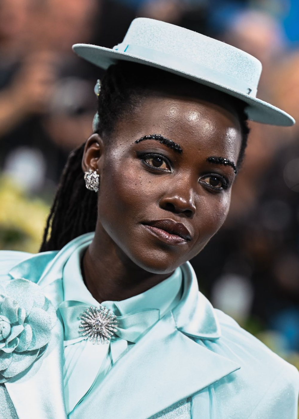 Uma pessoa com chapéu e terno azul claro adornado, possivelmente em um evento como o Met Gala 2025.