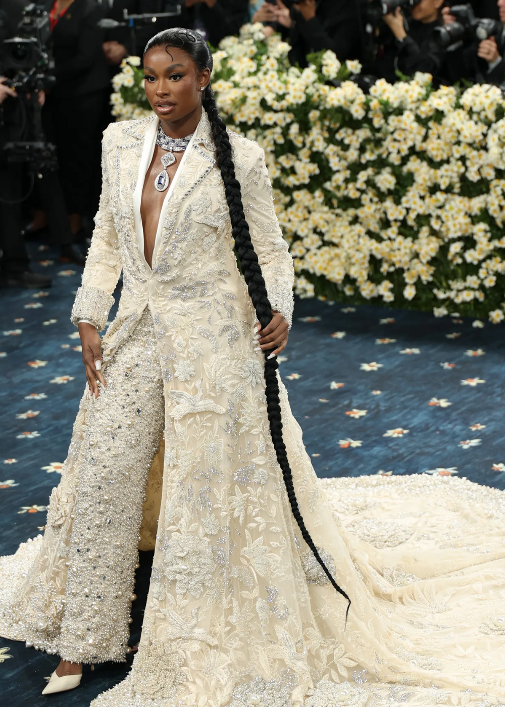 Vestido luxuoso bordado em evento com tema de flores, destacando-se no tapete do Met Gala 2025.