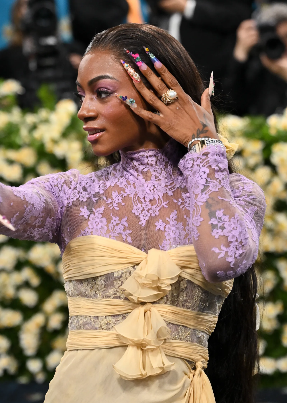Participante no Met Gala 2025 usa vestido de renda lilás, mostrando unhas decoradas.