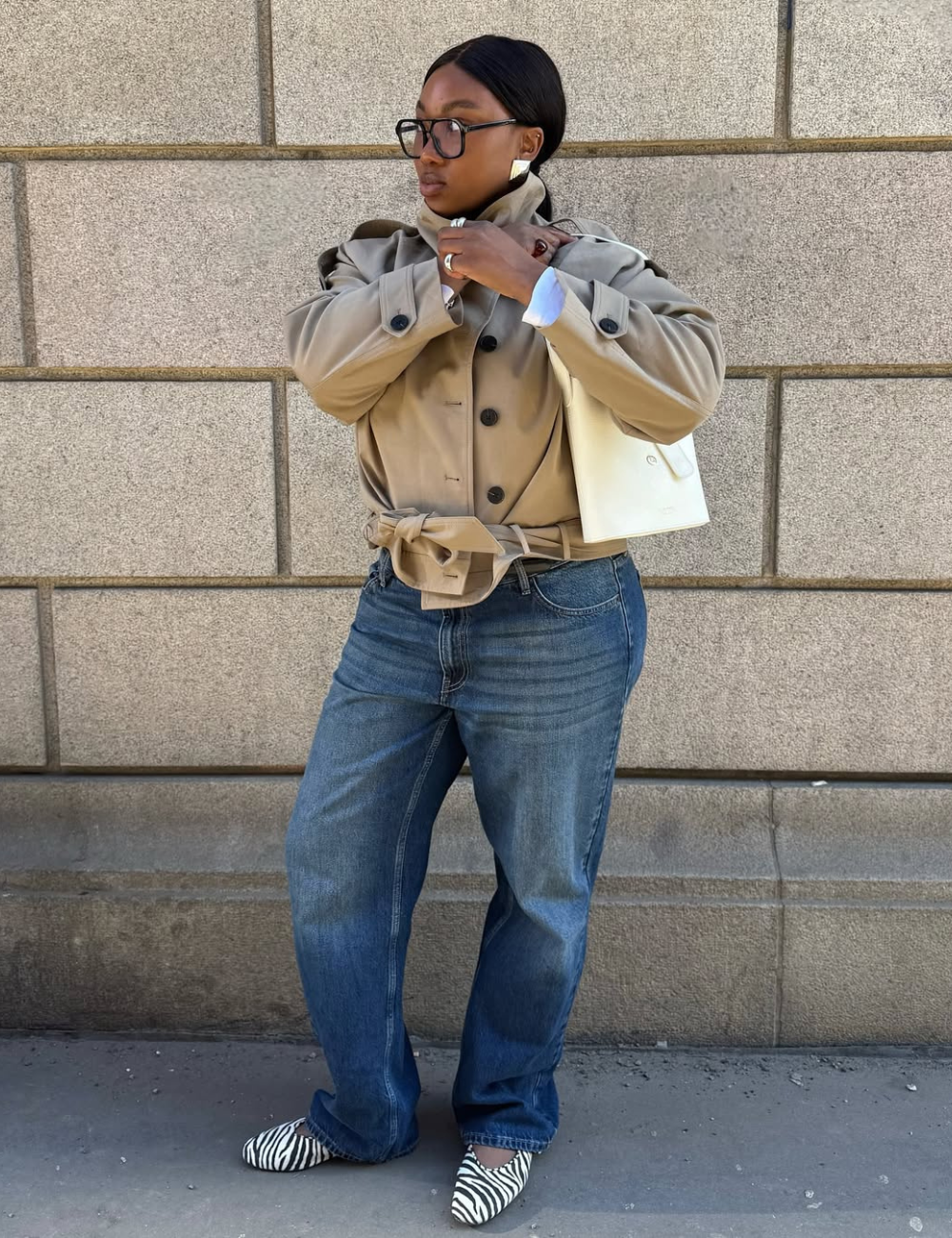 Casaco bege estiloso com cinto e calça jeans. Sapatos com estampa animal completam a tendência moderna.