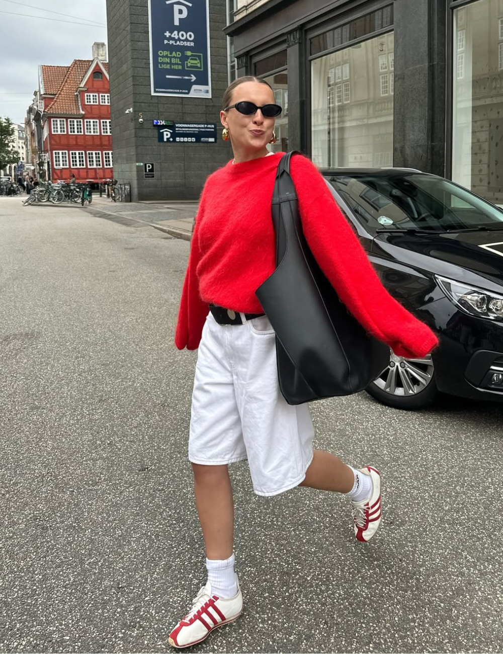 Pessoa com estilo moderno, vestindo suéter vermelho e bermuda branca, reflete peças estilosas e tendência do momento.