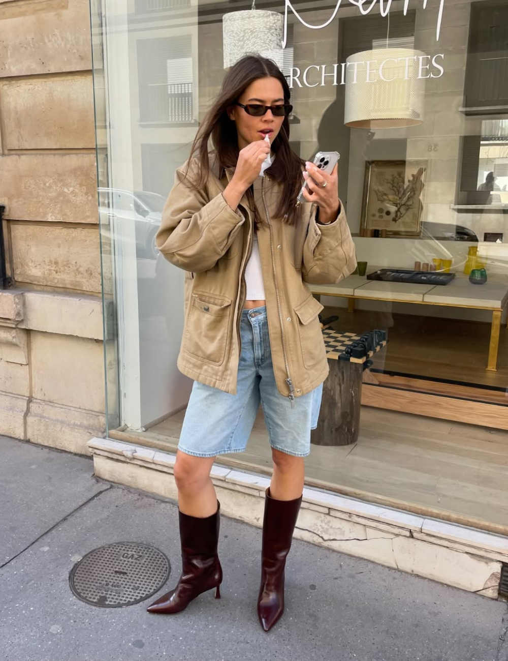 Mulher em look casual com jaqueta estilosa e bermuda jeans, seguindo tendência de moda. Ela usa botas marrons.