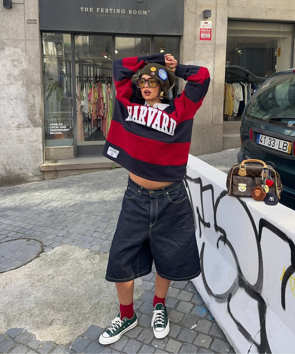 Pessoa em frente a uma loja vestindo uma blusa de listras, saia jeans e tênis femininos estilosos verdes.