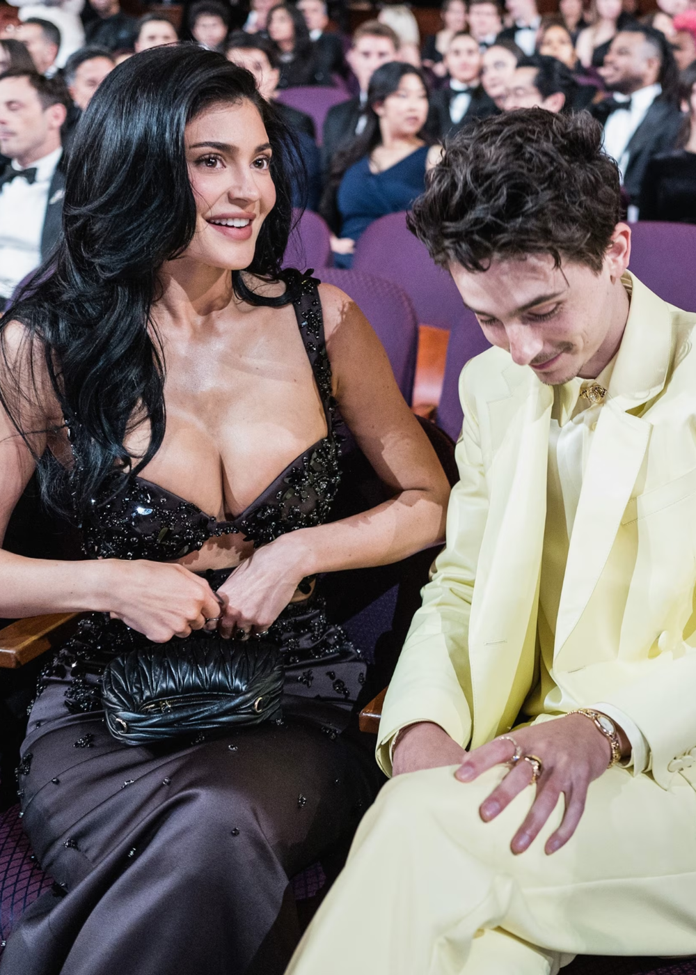 Kylie Jenner e Timothée Chalamet no Oscar, uma de vestido preto e a outra de terno claro, sorrindo e conversando.