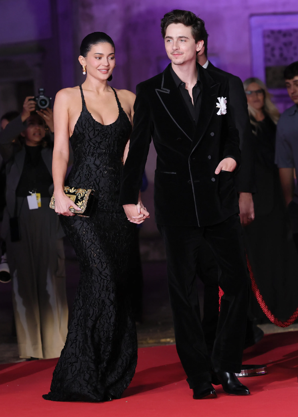 Kylie Jenner e Timothée Chalamet caminham de mãos dadas em um tapete vermelho, cercado por câmeras e admiradores.