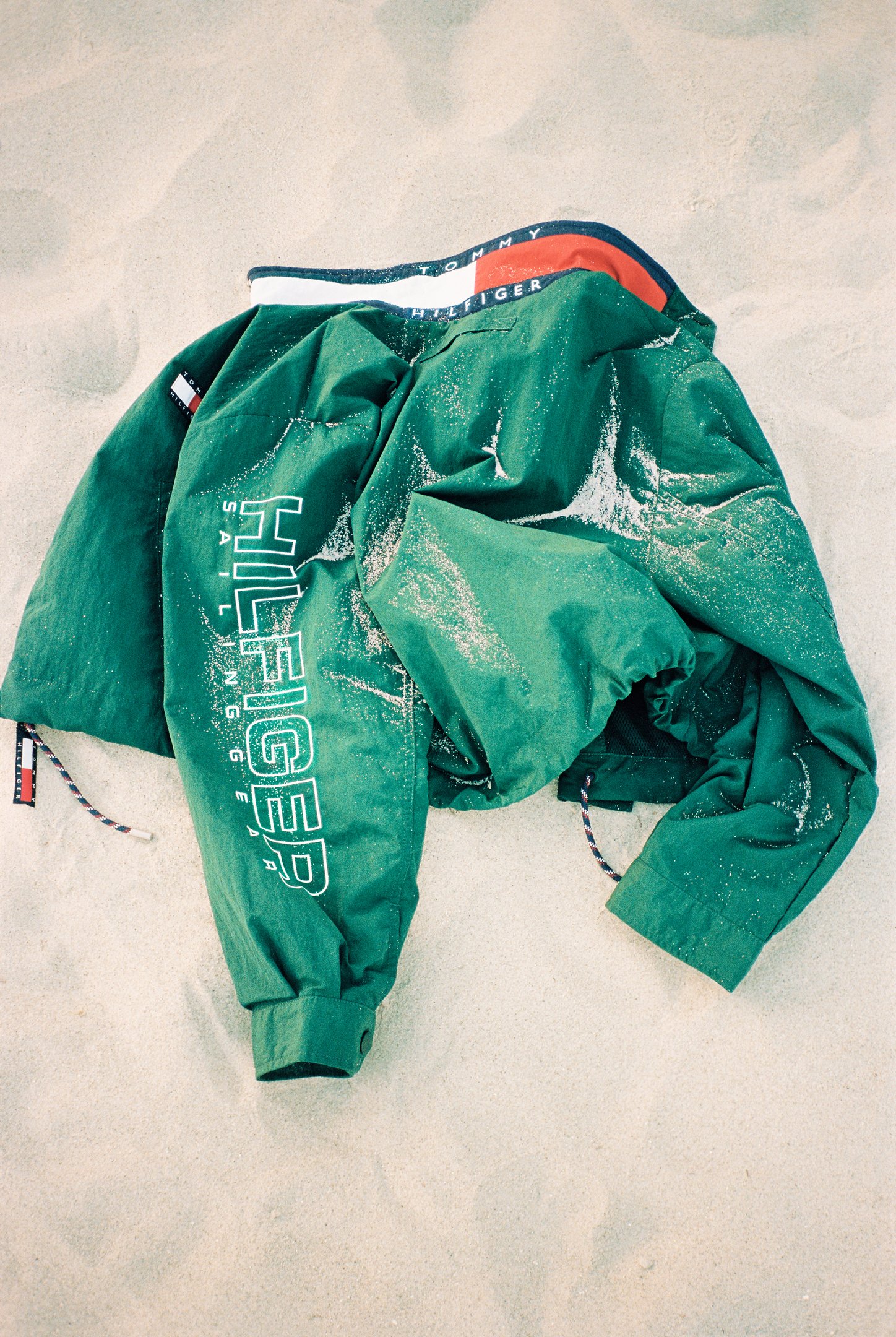 Casaco verde na areia, estilo náutico, com detalhes de corda e marca visível, em mood fishermancore.