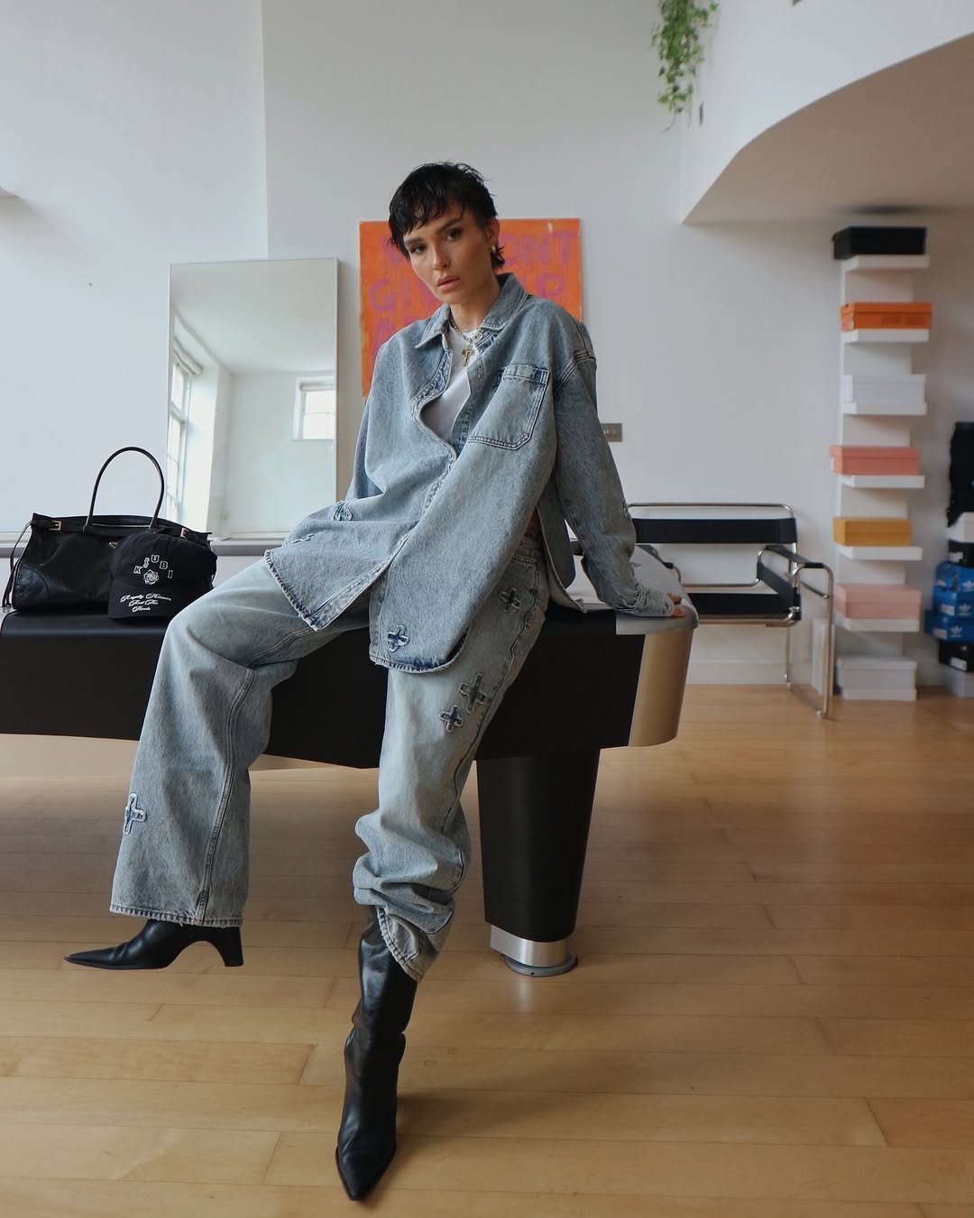 Pessoa com conjunto oversized jeans em espaço moderno, usando truque de styling fácil com botas pretas.