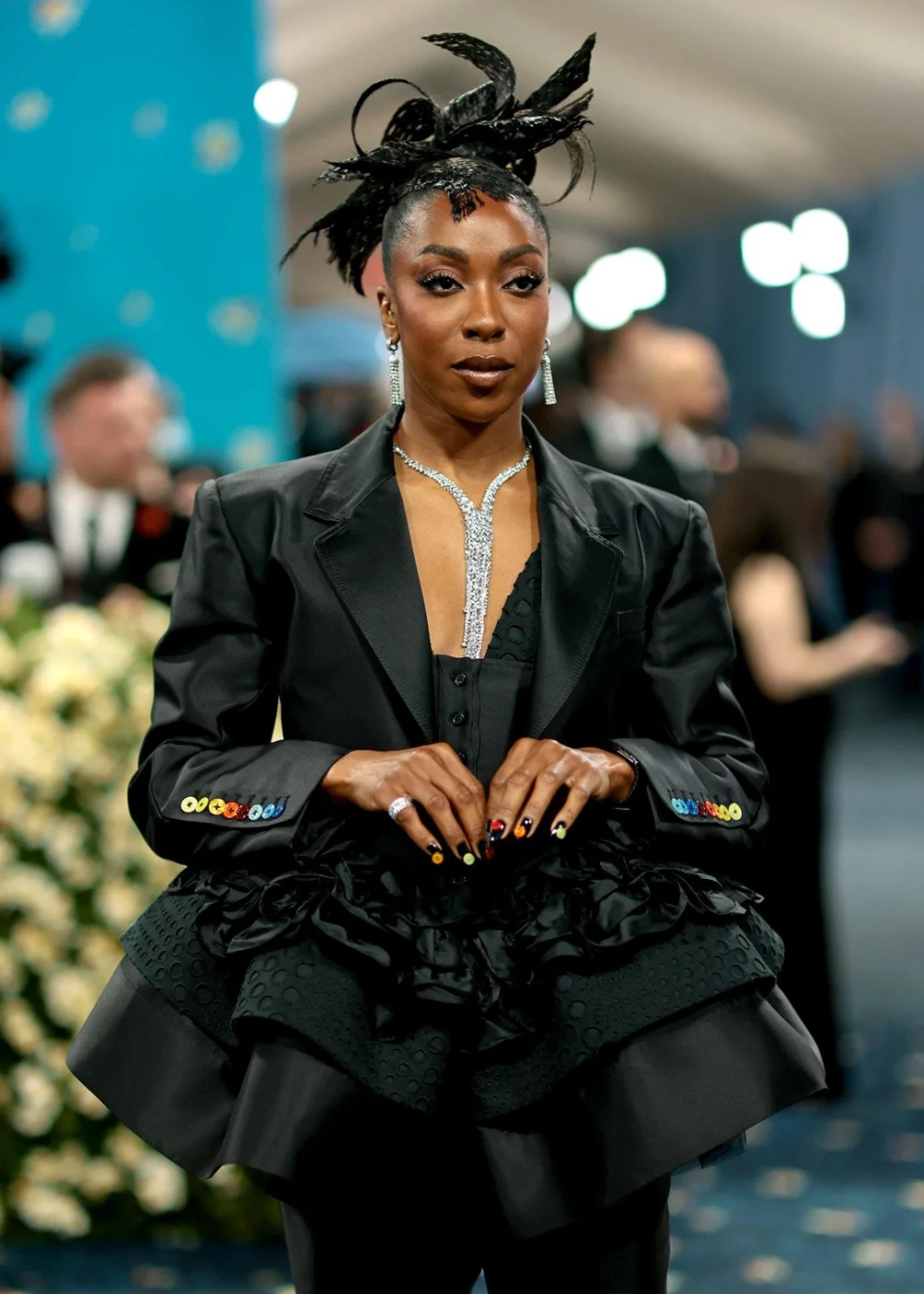 Pessoa com cabelo estilizado e roupa preta sofisticada. As unhas maximalistas chamam atenção pelos detalhes brilhantes.