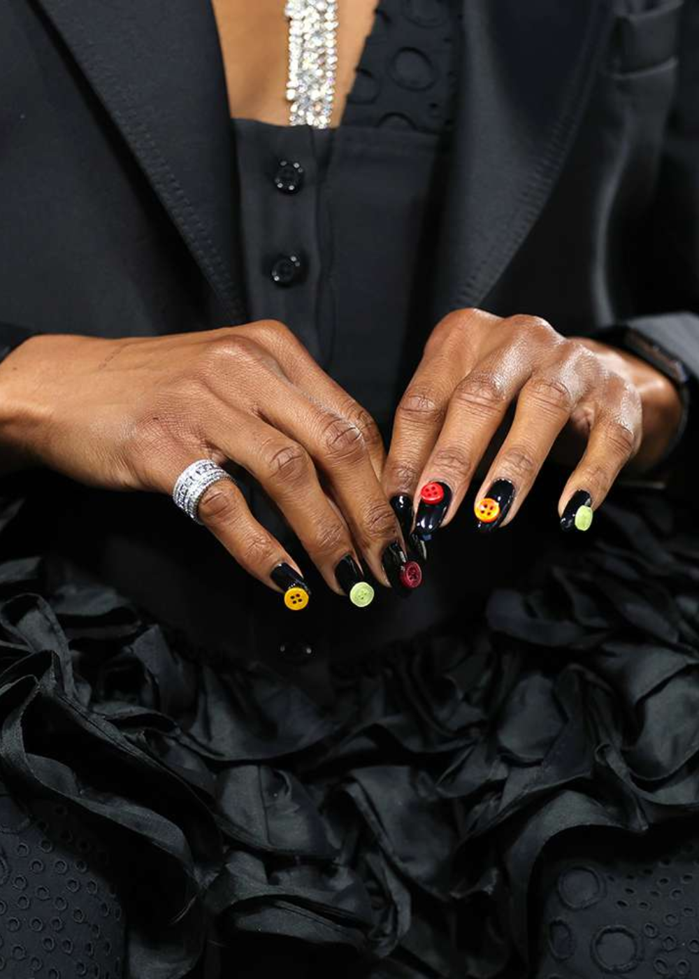 Unhas decoradas com botões coloridos sobre esmalte preto, estilo unhas maximalistas.
