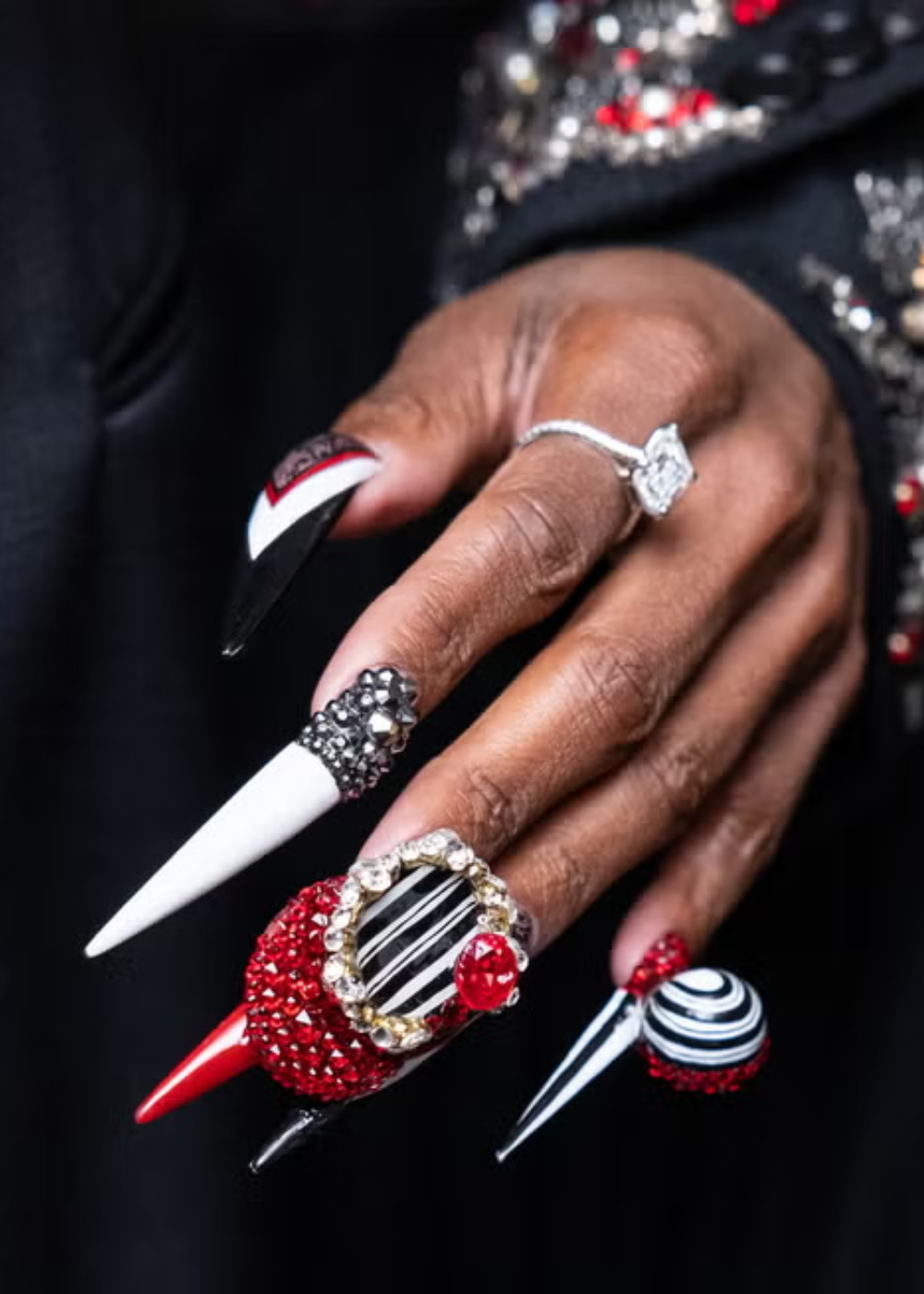 Unhas maximalistas com adornos em vermelho, preto e branco, realçando brilho e textura extravagante.