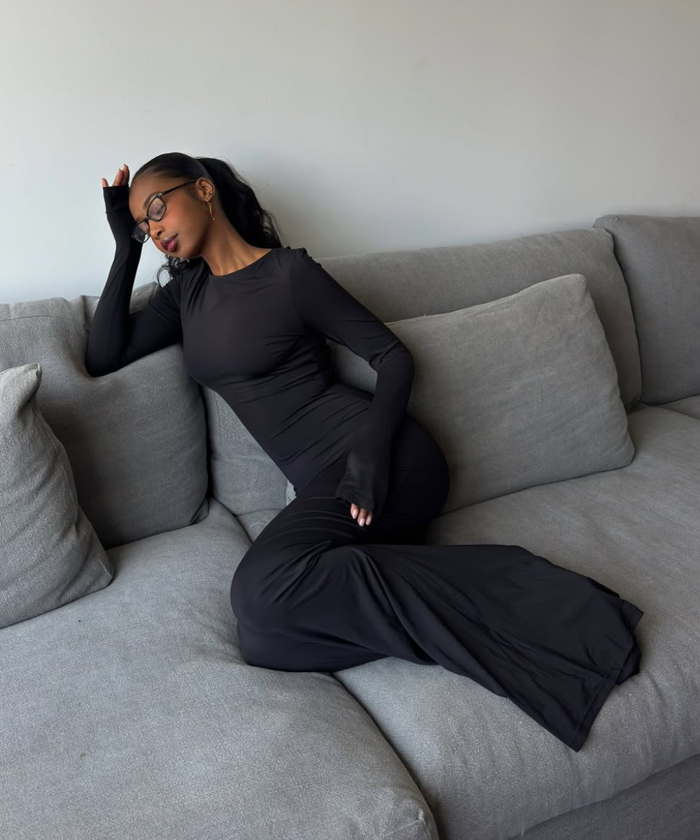 Pessoa relaxa em sofá usando vestido chique preto justo, segurando a cabeça com uma mão.