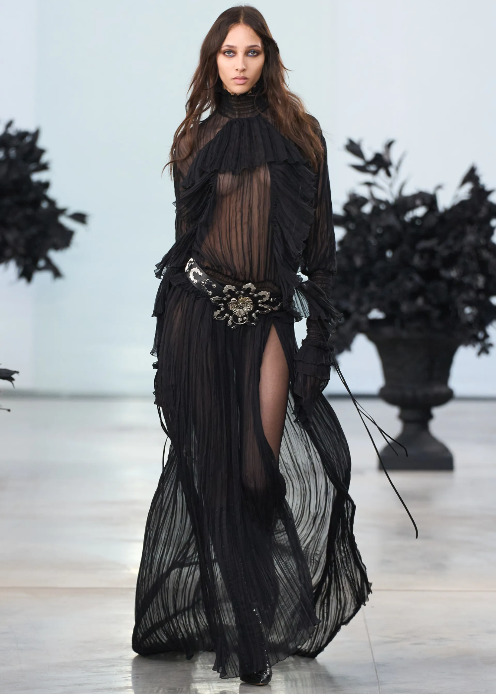 Modelo com vestido preto transparente e cinto decorado em passarela, estilo boho.